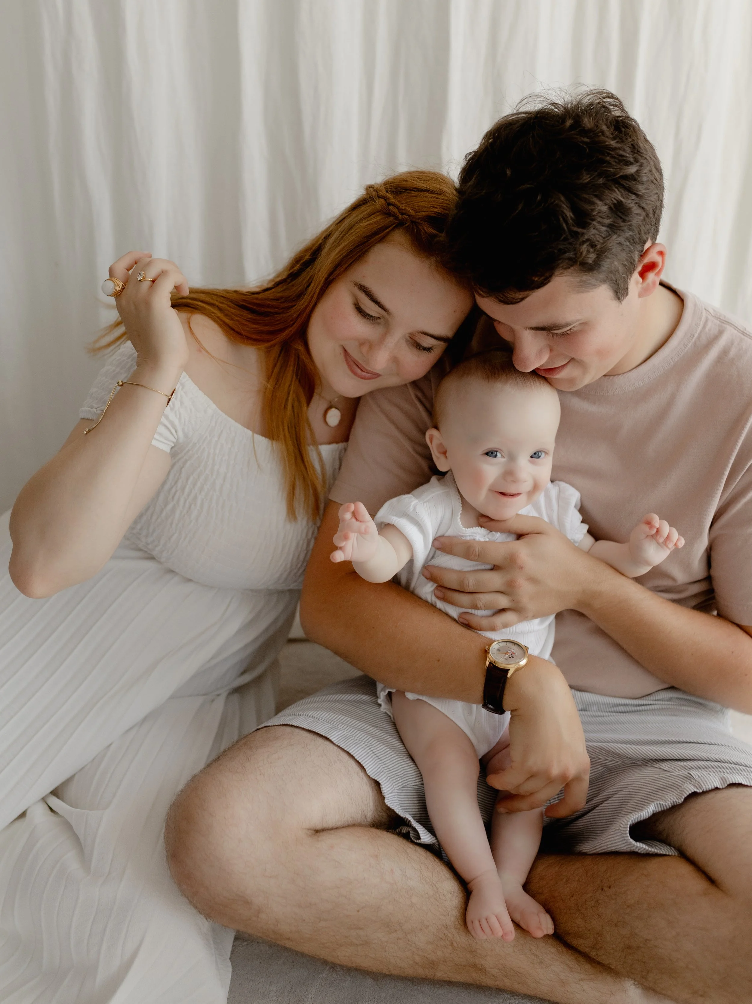 Mum and dad sitting together with their smiling baby during a family photography session in the studio.