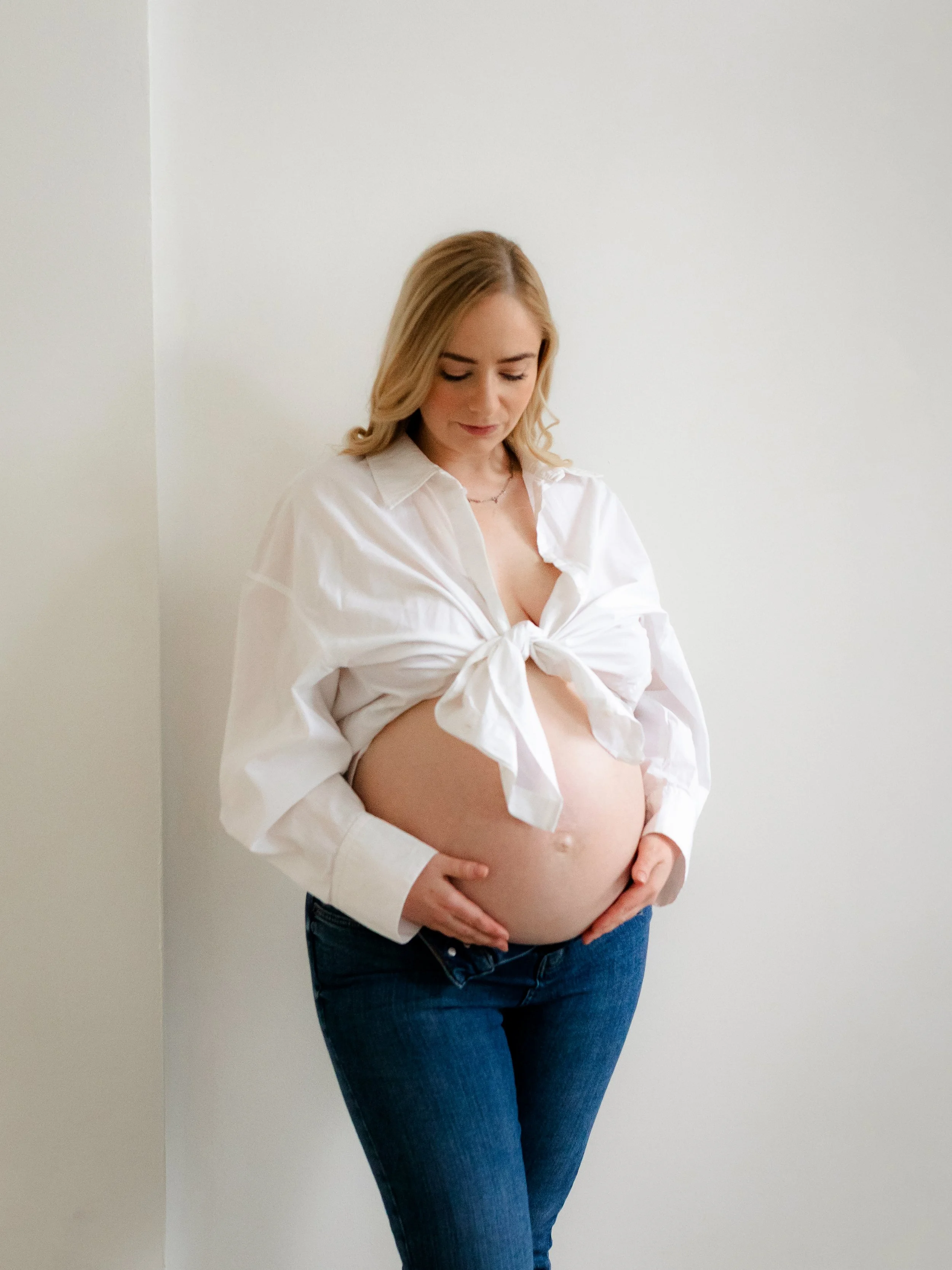 Natural studio maternity portrait of an expectant mother in a white shirt and jeans