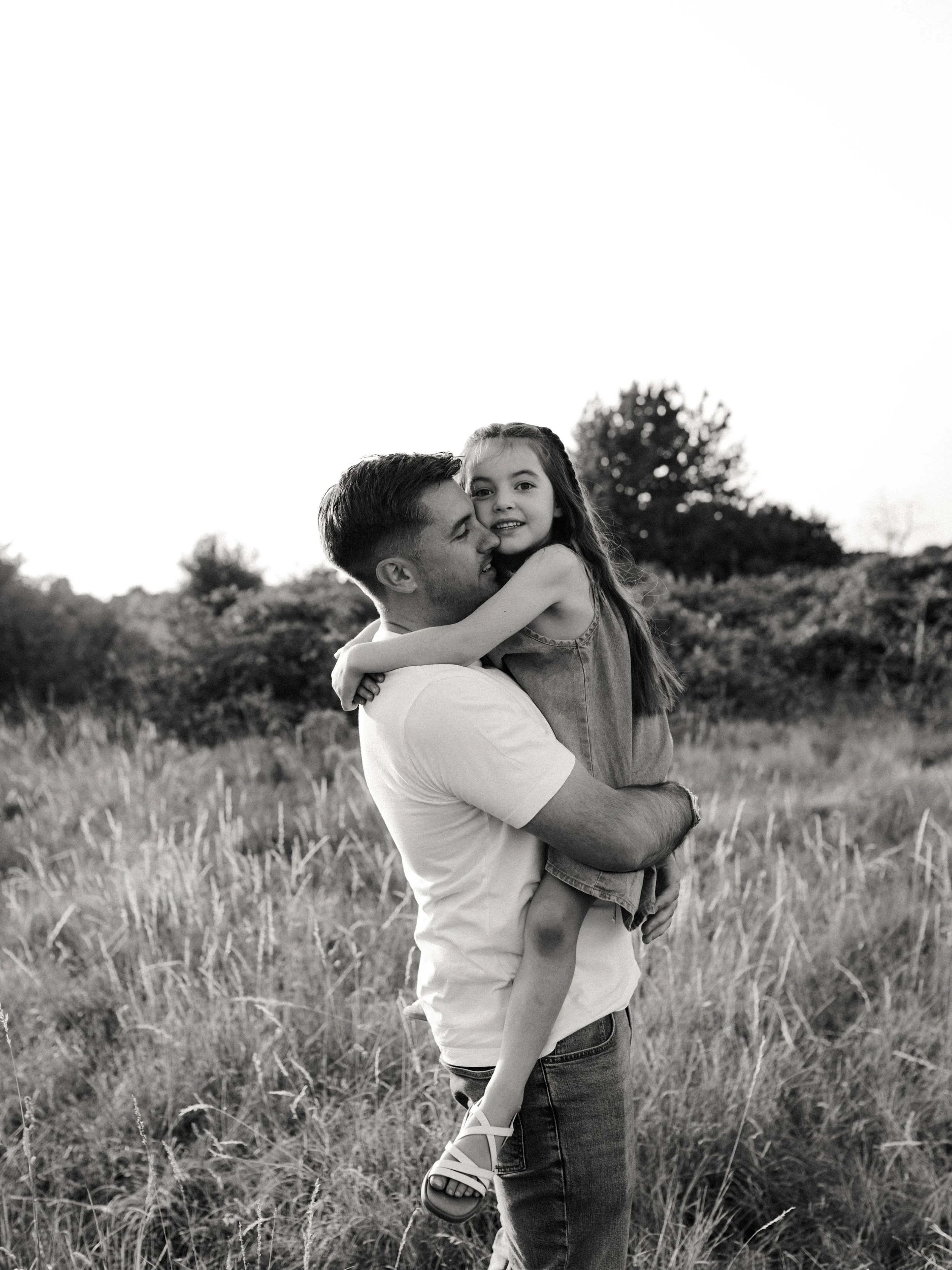 Dad holding and cuddling his daughter during a natural outdoor family photography session.