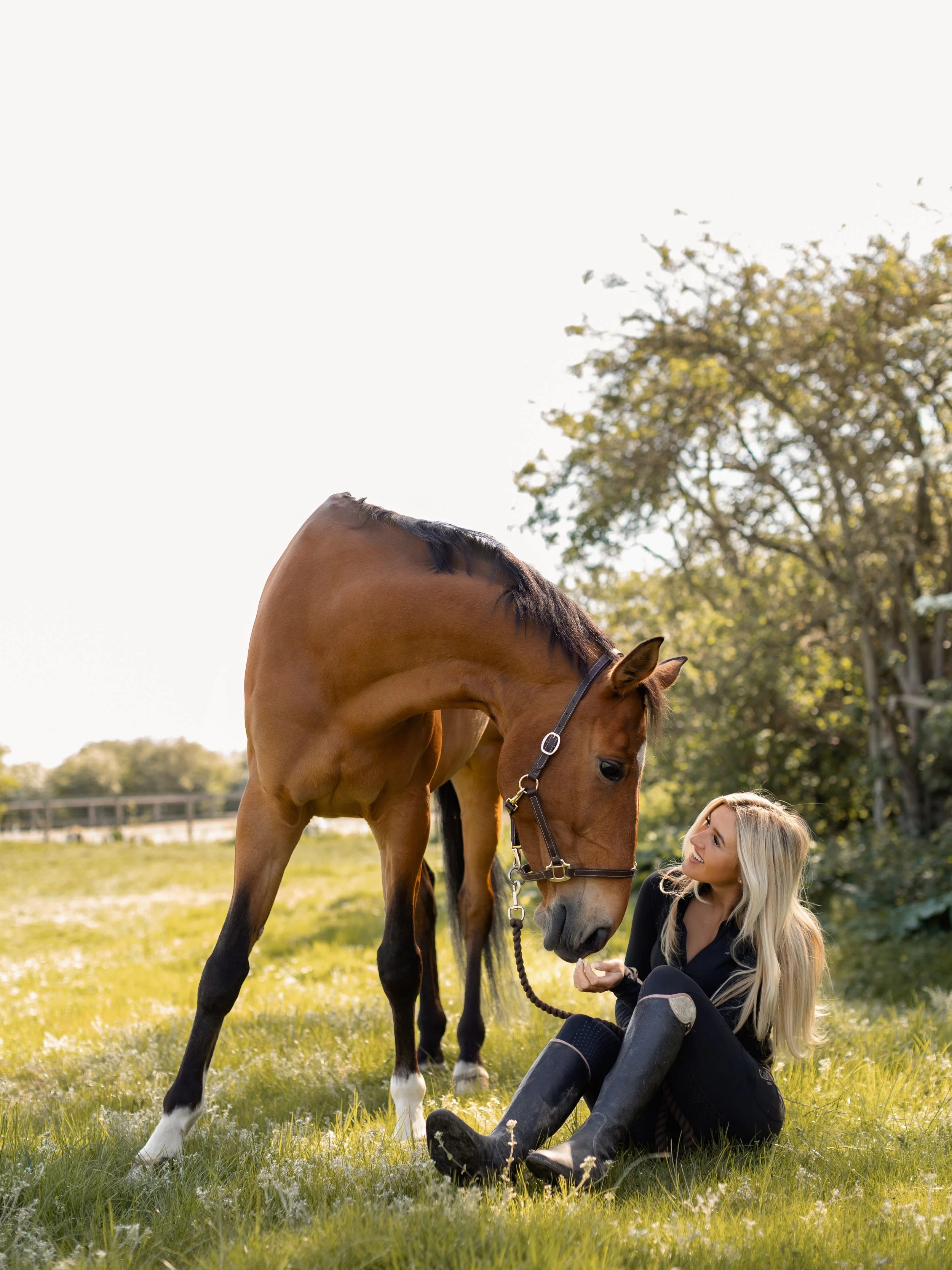 Woman sitting beside her horse in a field during a natural equine photography session in Essex.