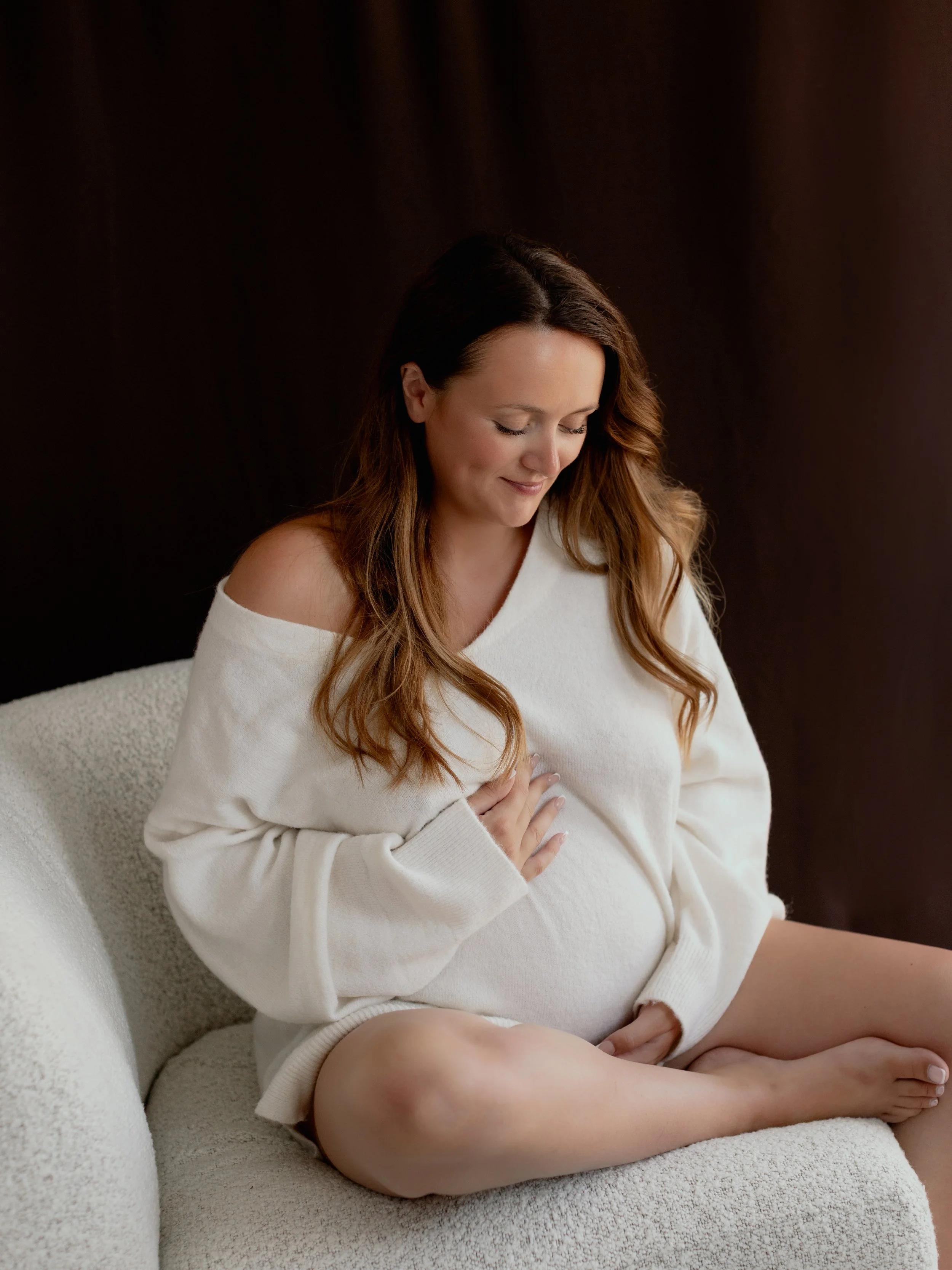 Pregnant woman seated in a cream chair during a maternity photography session in South Ockendon, Essex