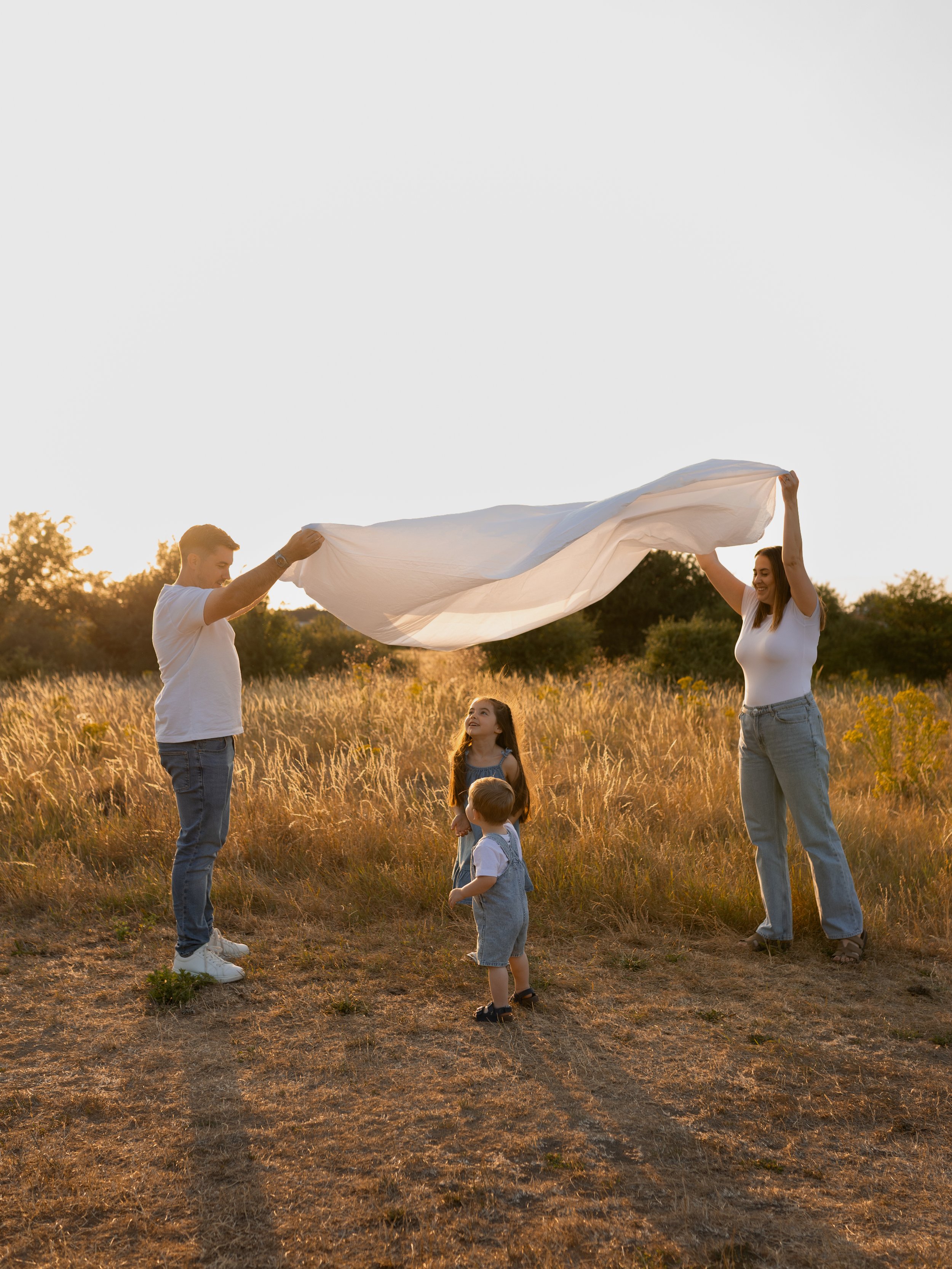 Family playing together with a white sheet in a field at sunset during an outdoor family photography session in Essex.