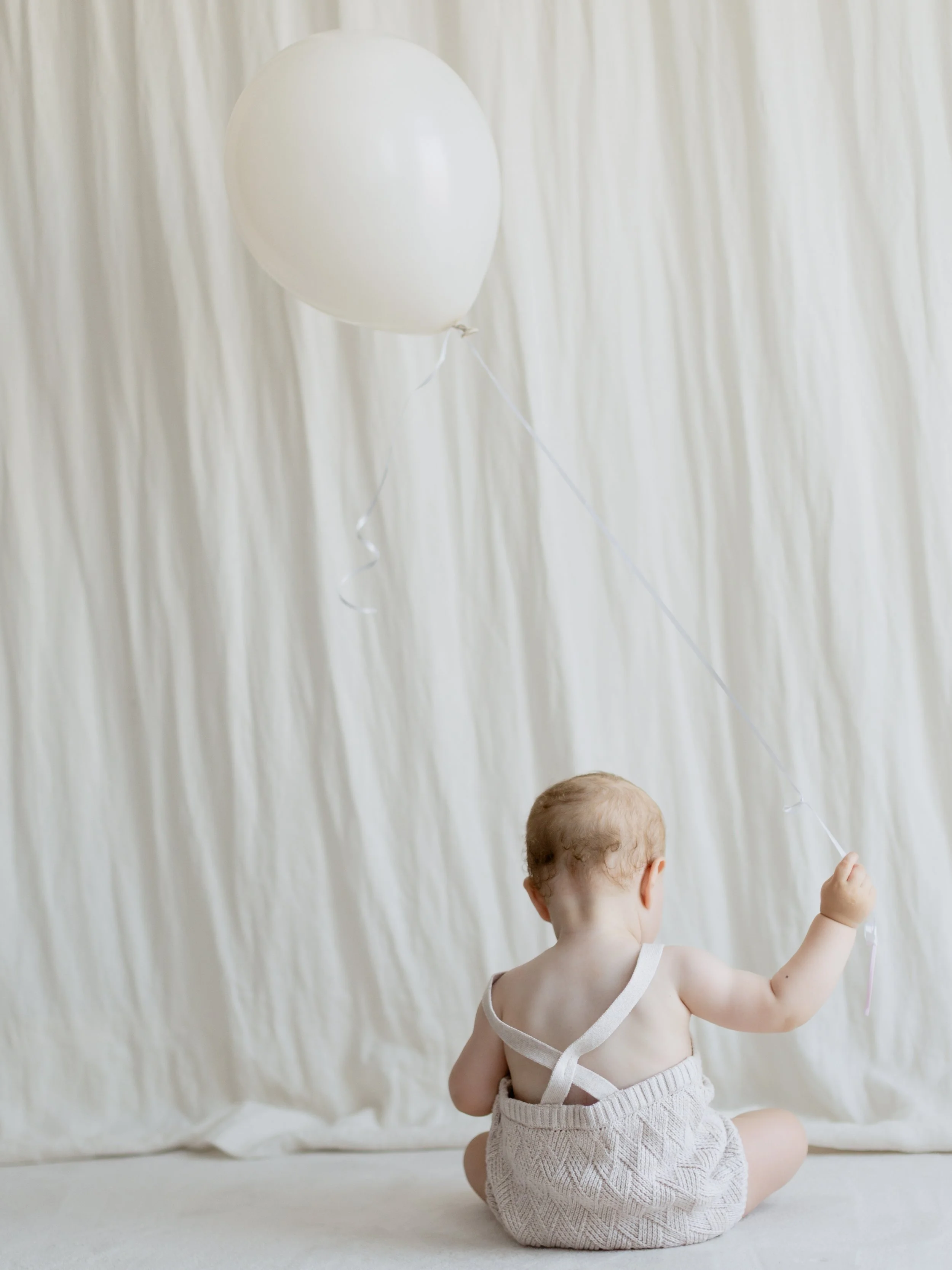 Baby holding a white balloon during a simple first birthday studio photoshoot