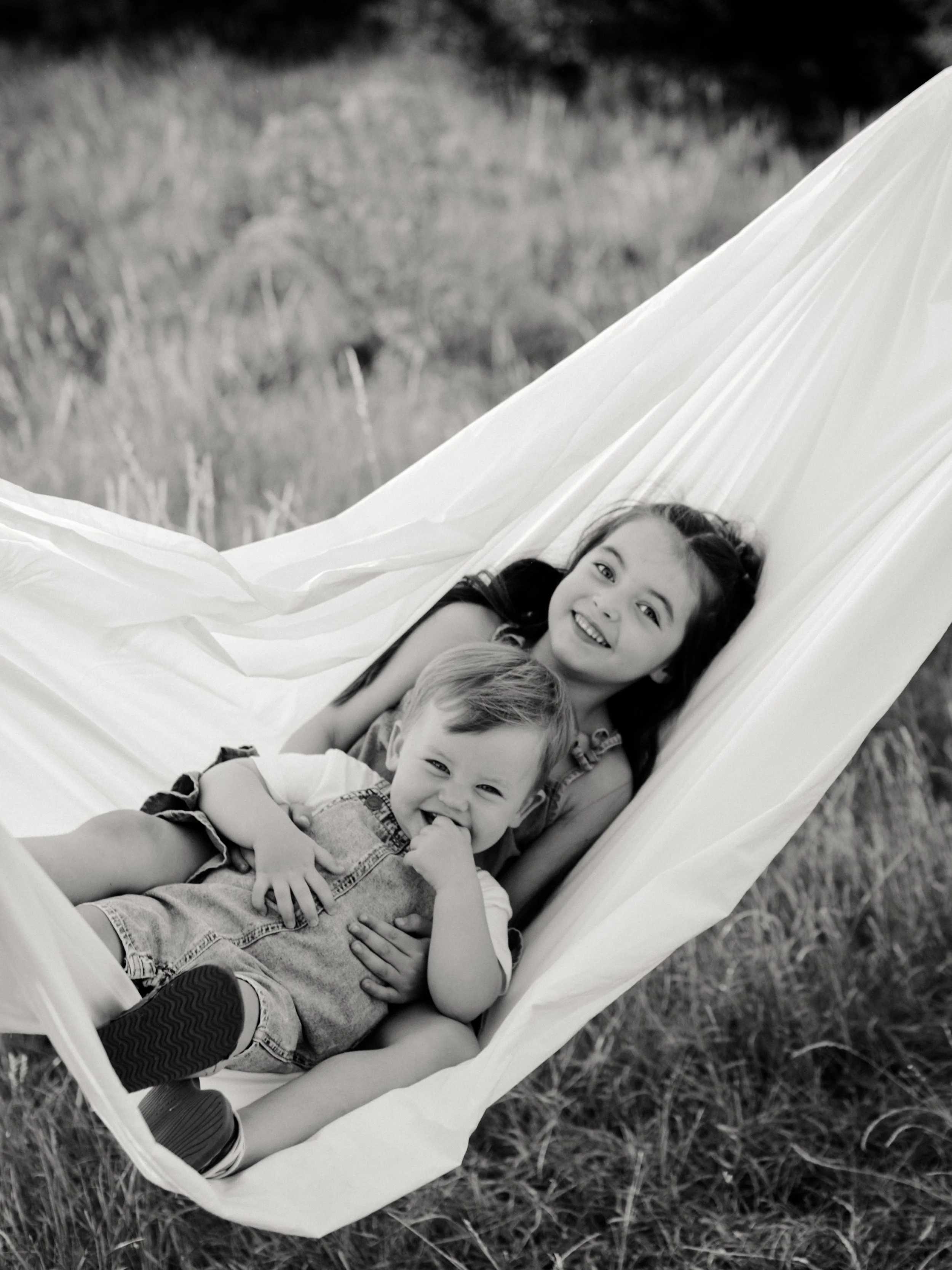 Brother and sister laughing together in a white sheet during a playful outdoor family session.