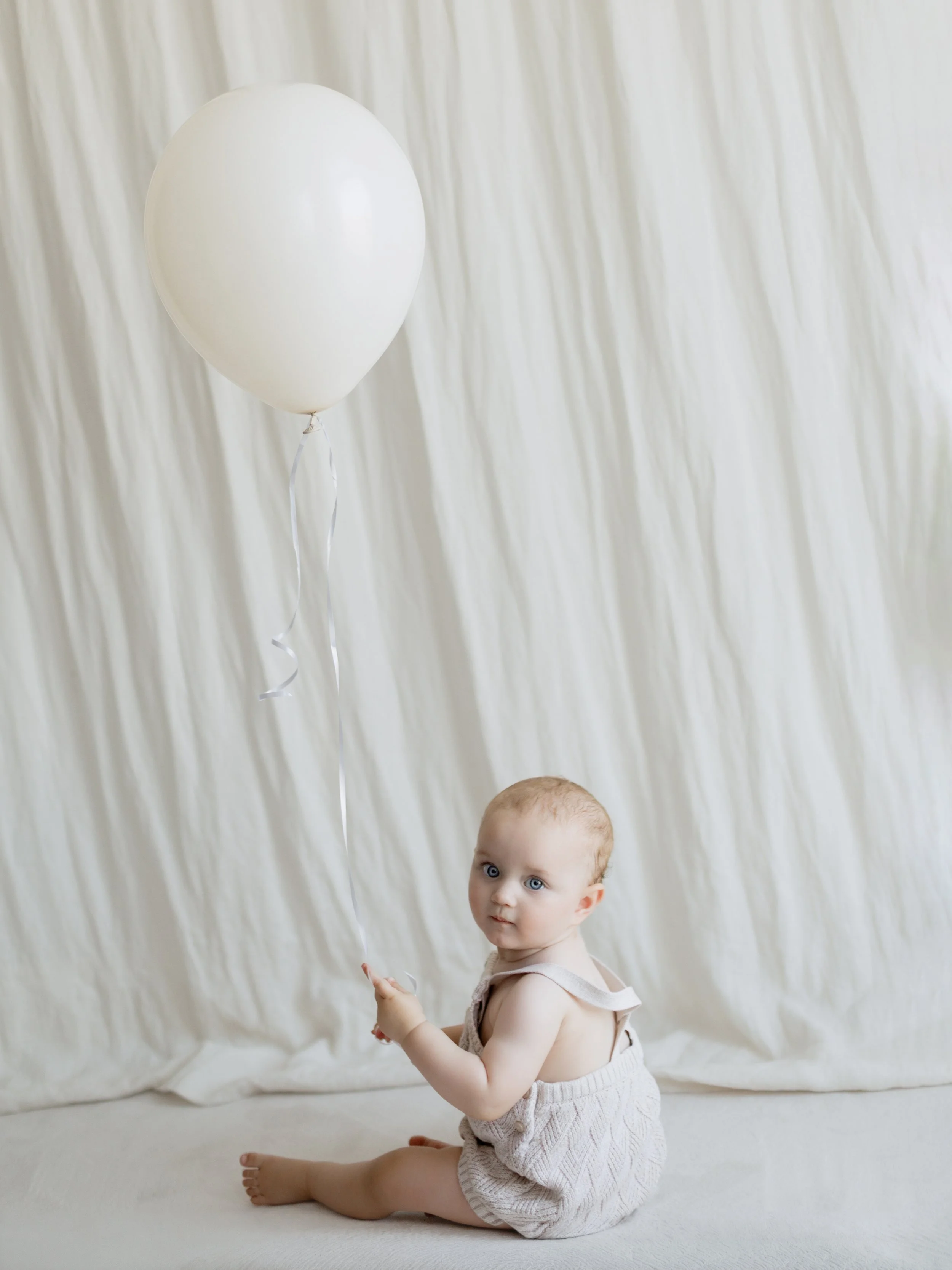 Baby sitting with a white balloon during a first birthday portrait session