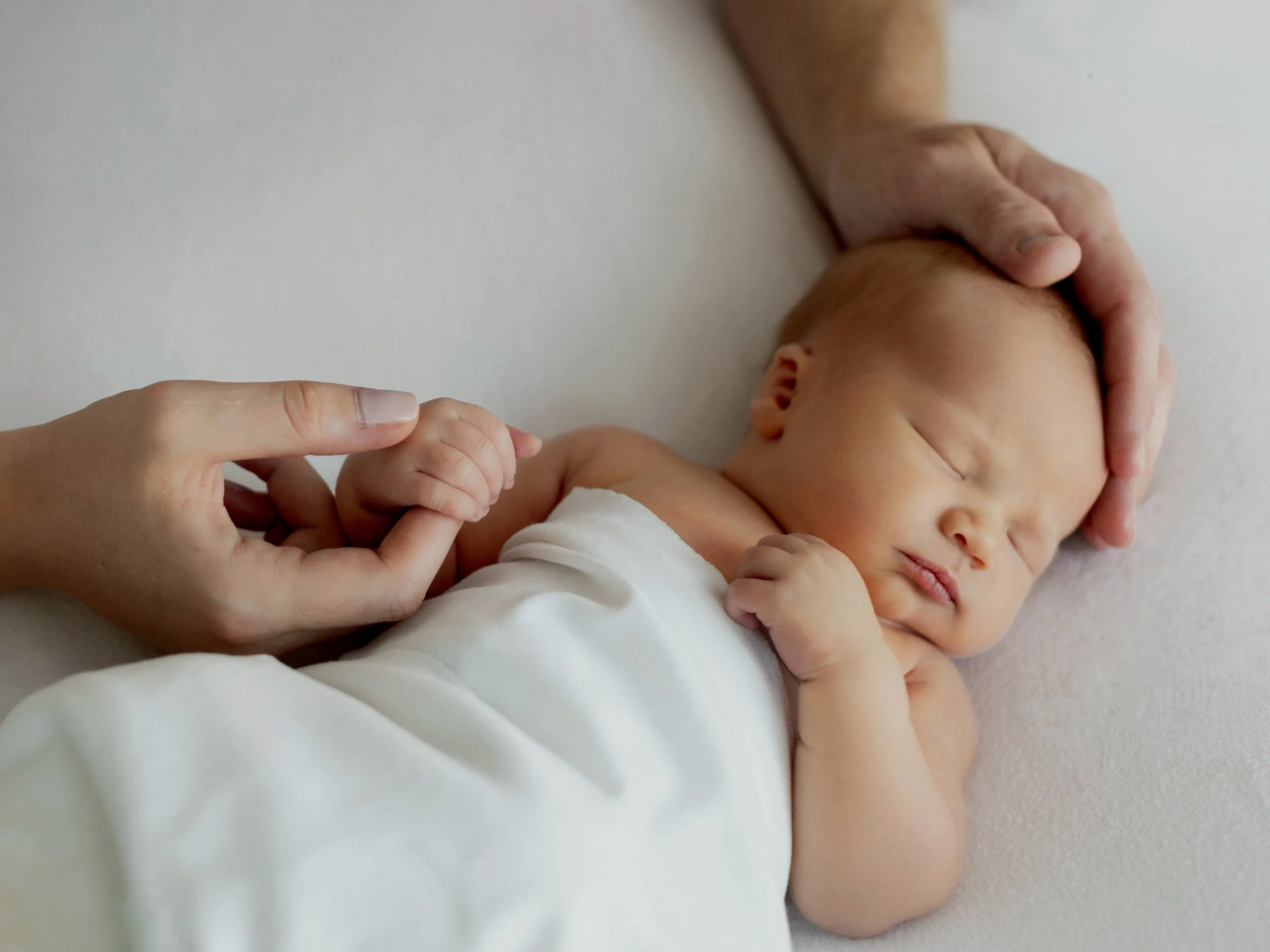 Sleeping newborn baby held gently by their parents during a studio newborn session