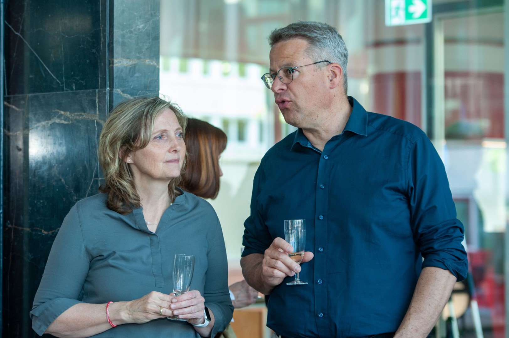 Ein Mann und eine Frau unterhalten sich bei einer Feier, beide halten Gläser mit Sekt.