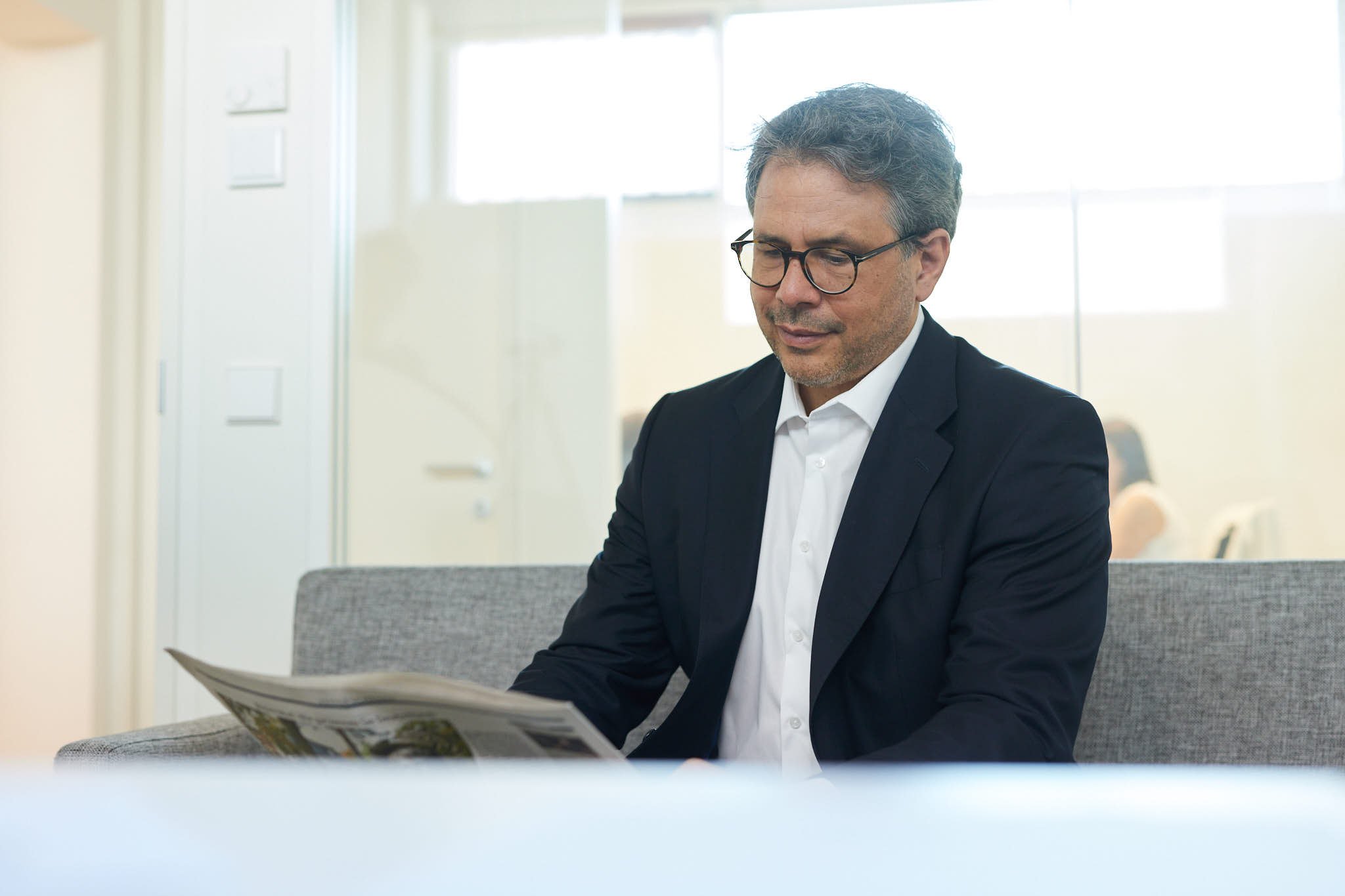 RA Jan Schabbeck von VSZ Rechtsanwälte sitzt in einem hellen Raum und liest eine Zeitung, während er an einem Tisch sitzt.