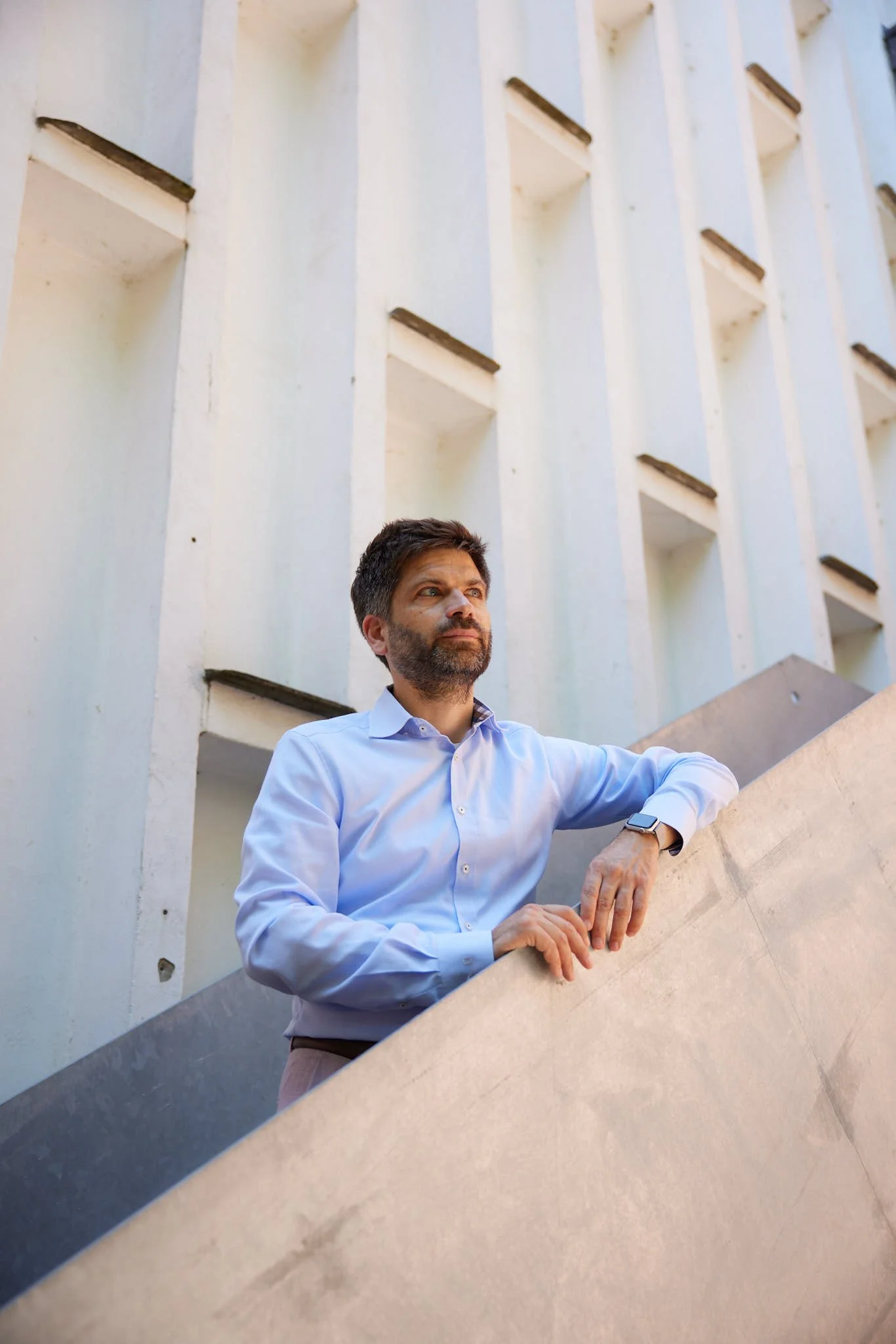 Karsten Mühlsteph von VSZ Rechtsanwälte auf einem Betonsockel vor einem modernen Gebäude mit quadratischen Fenstern, Blick nach oben gerichtet.