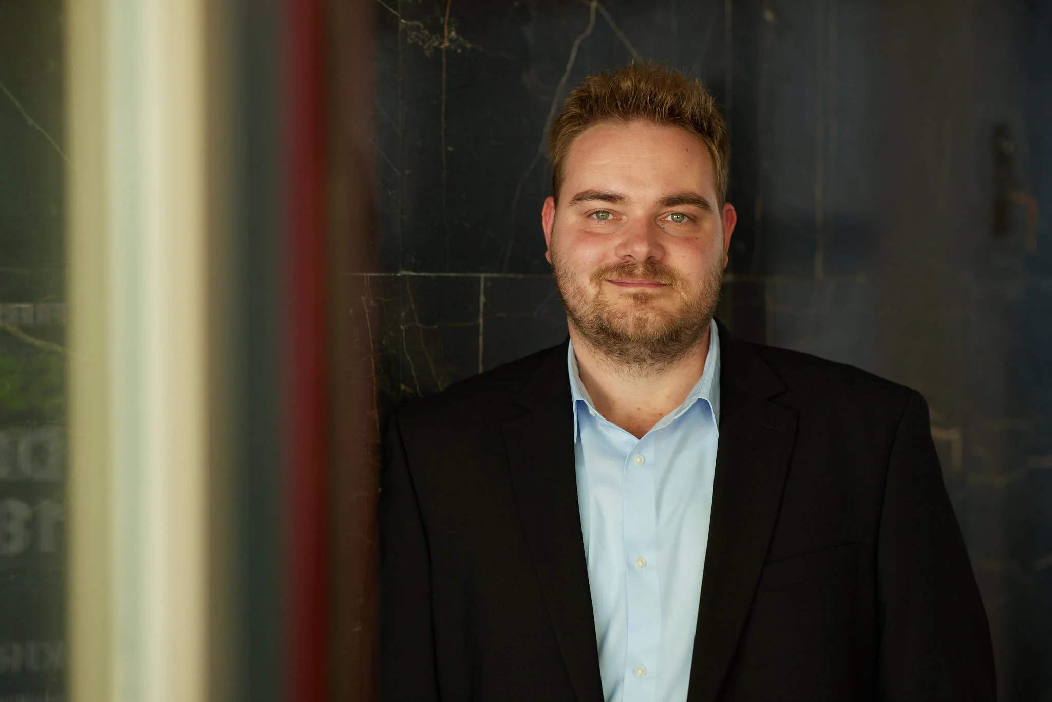 RA Seegert von VSZ Rechtsanwälte, trägt einen schwarzen Anzug und hellblaues Hemd, sitzt auf einem schwarzen Marmorboden, hinter ihm eine dunkle Wand.