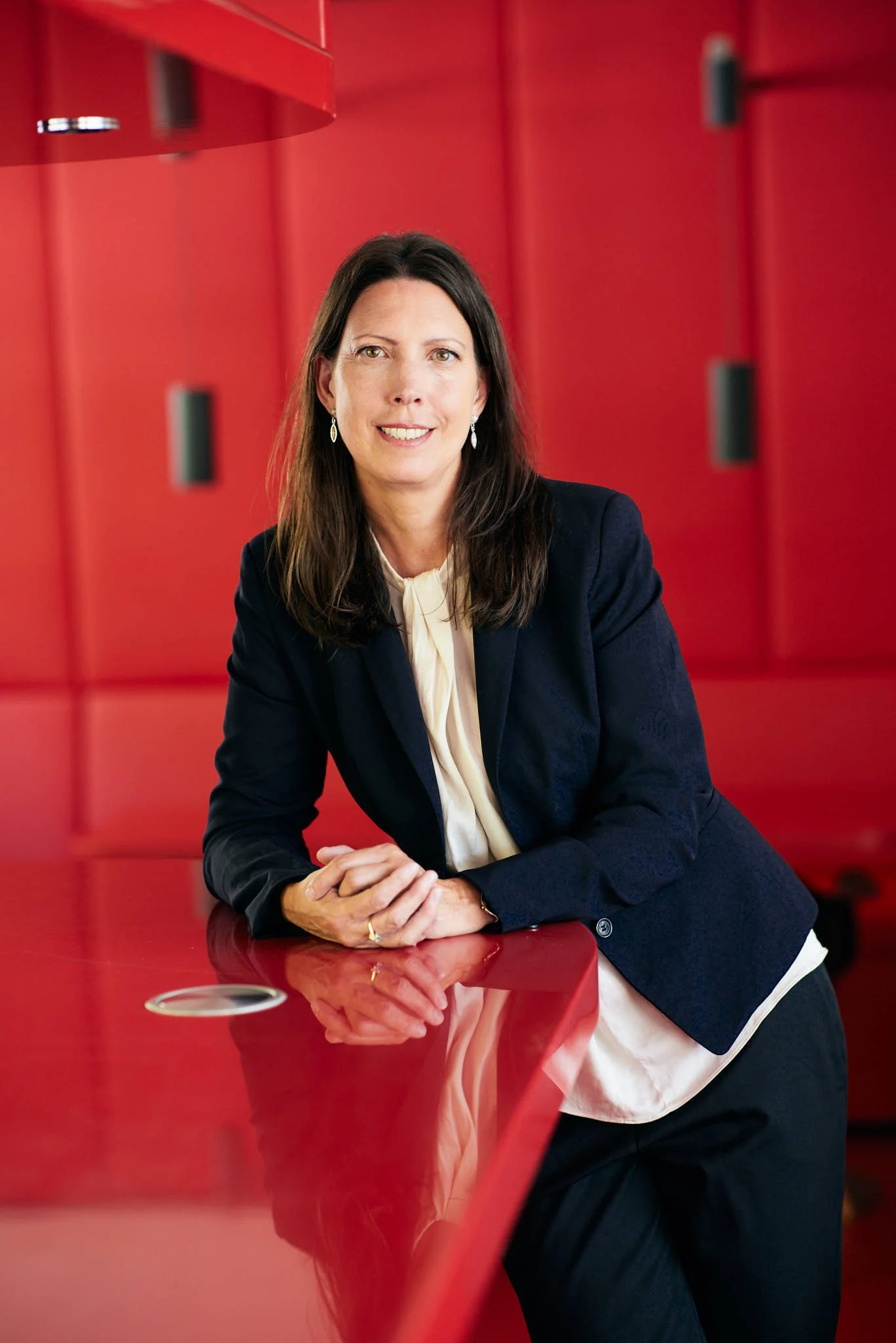 RAin Silke Ahlborn von VSZ Rechtsanwälte, die lächelt, sitzt an einem roten Tisch, trägt einen schwarzen Blazer und einen weißen Bluse, im Hintergrund rote Tapeten.