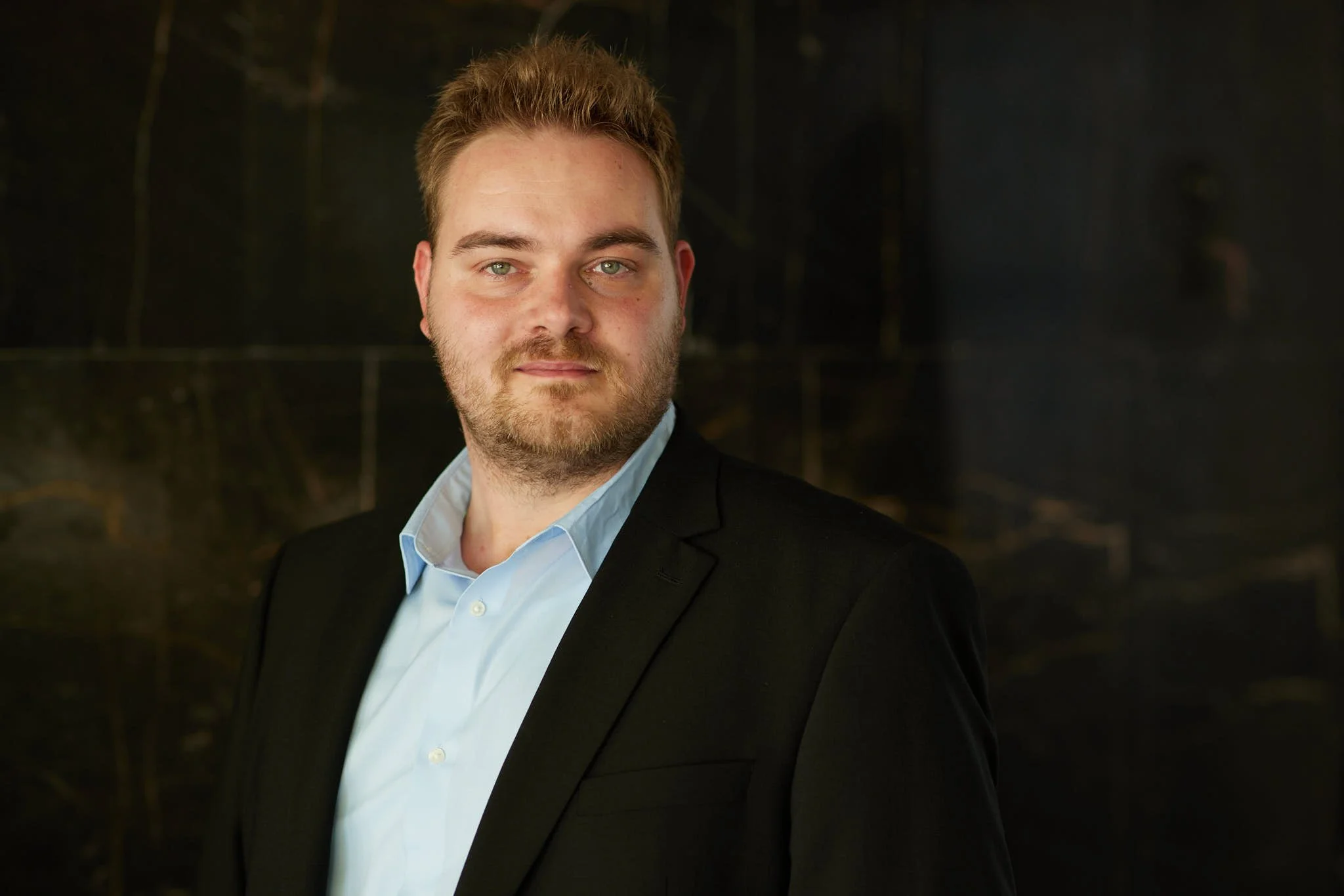 RA Seegert von VSZ Rechtsanwälte, trägt einen schwarzen Anzug und eine hellblaue Hemd vor dunklem Hintergrund.