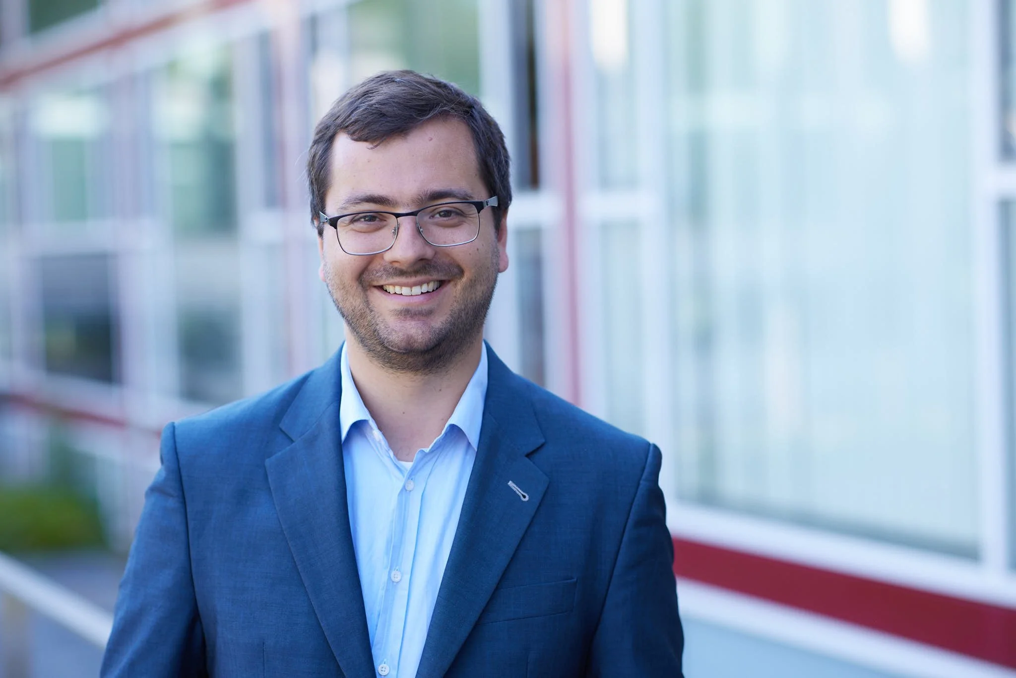 RA Boden von VSZ Rechtsanwälte steht vor einem modernen Gebäude mit großen Fenstern und rotem Akzent.