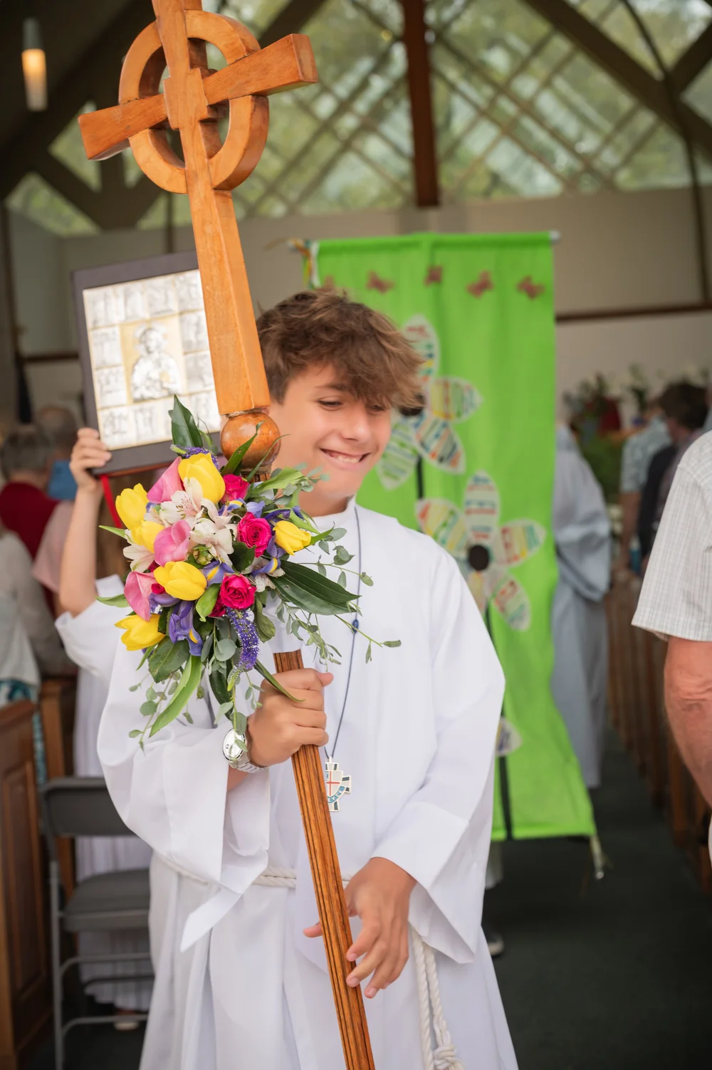 A young acolyte carrying the processional cross, dressed in flowers for Easter