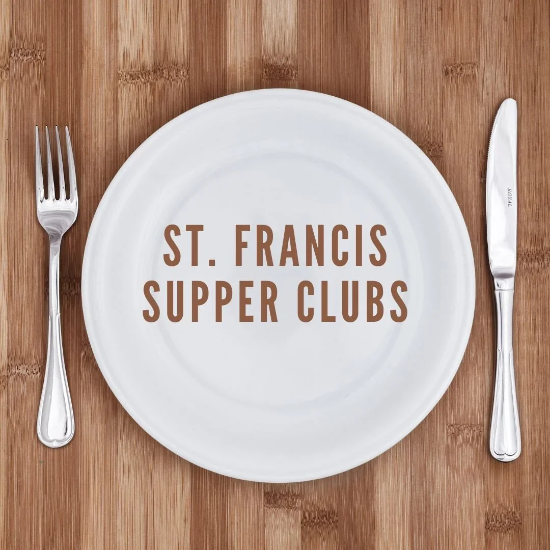 A white plate on a wooden table with the words 'St. Francis Supper Clubs' printed on it. A fork is placed to the left of the plate and a knife to the right.