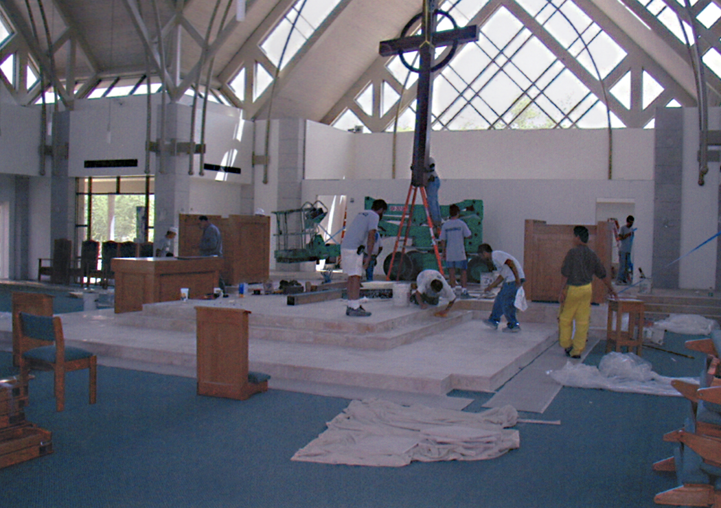 Workers installing a church altar inside a building with a high, glass-paneled ceiling.