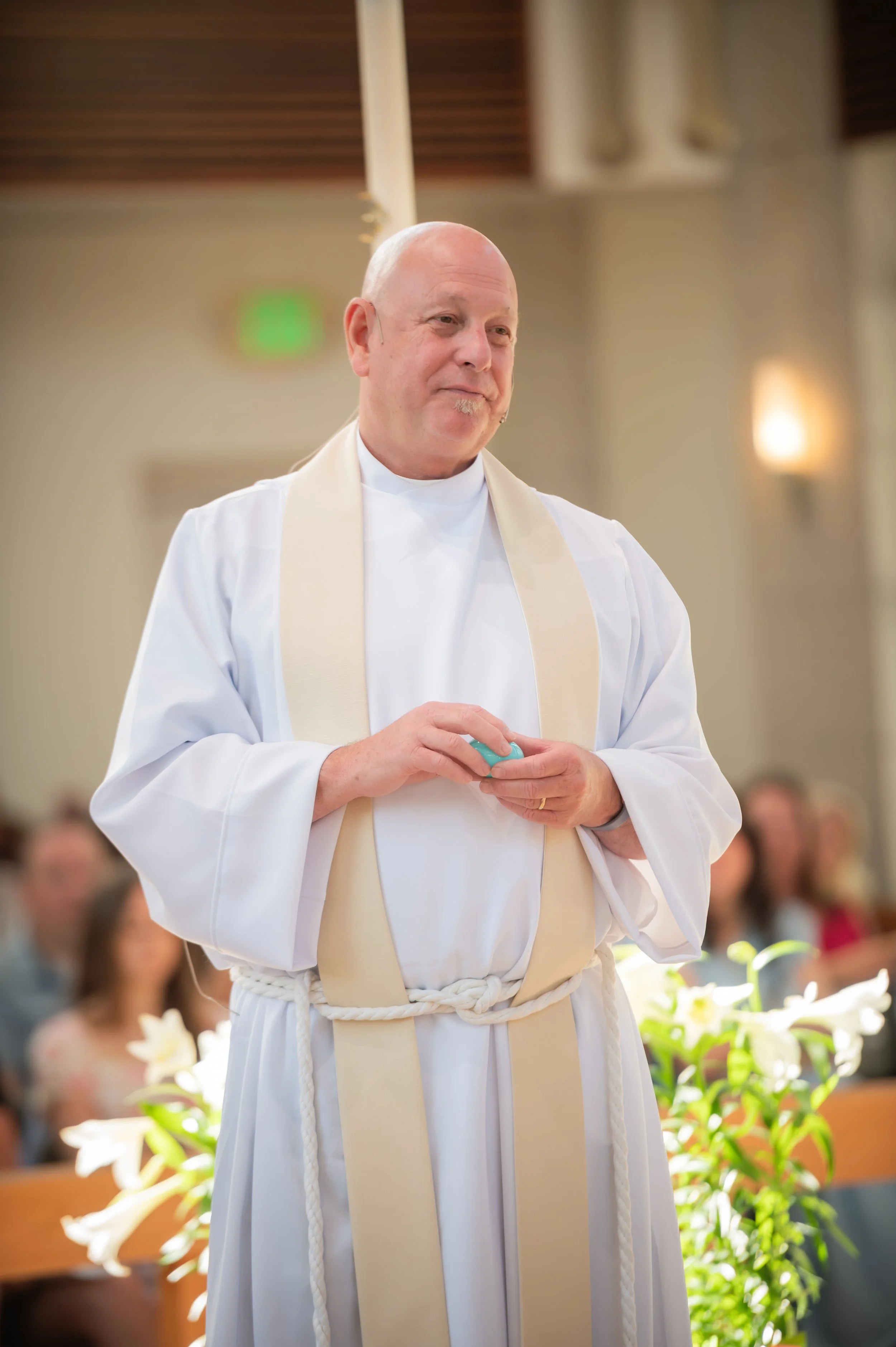 A smiling priest in white robes and vestments in worship service
