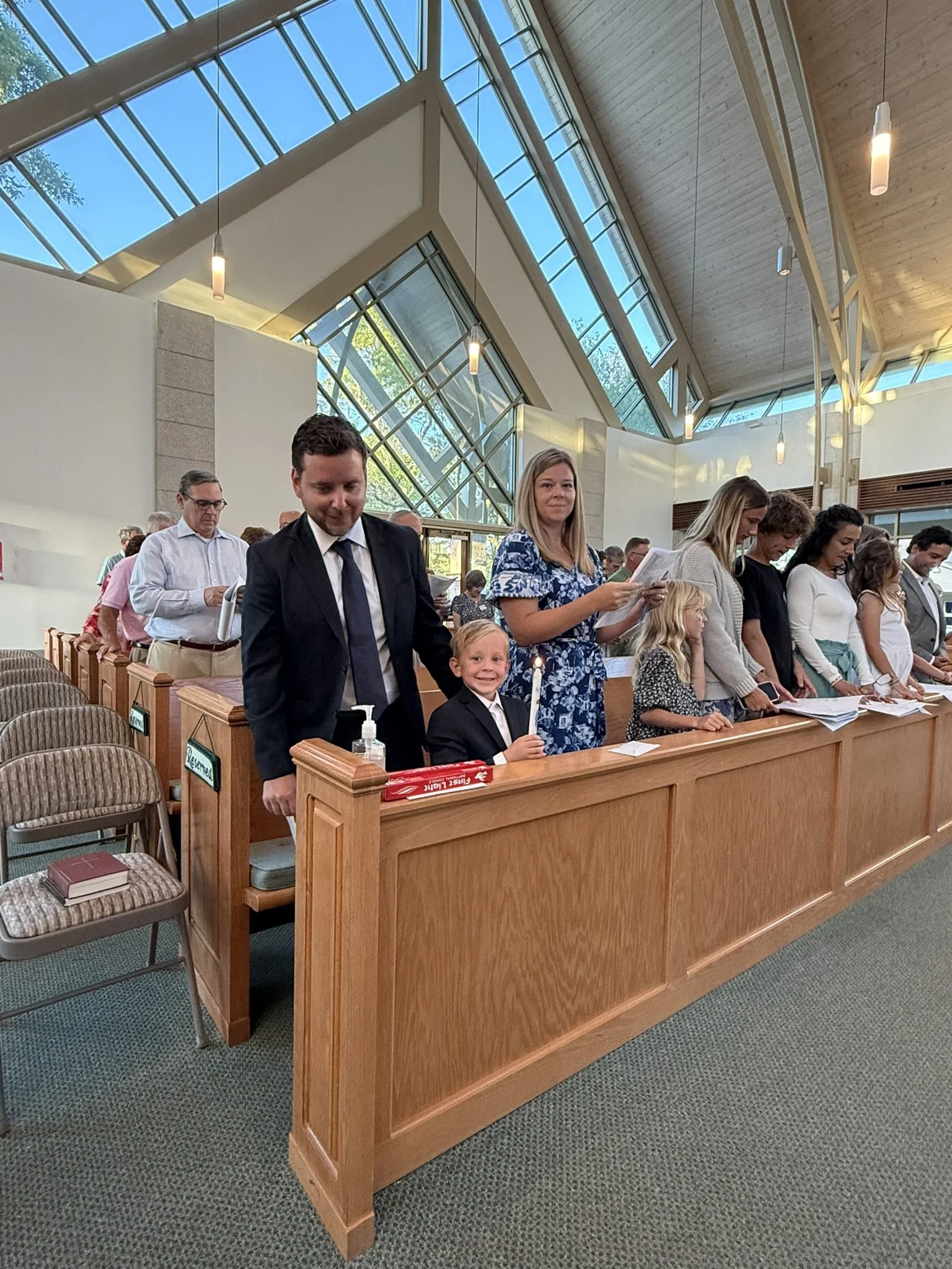 People gathered in a church for a religious service, standing at reflection or prayer, with a modern architectural interior and large glass windows.