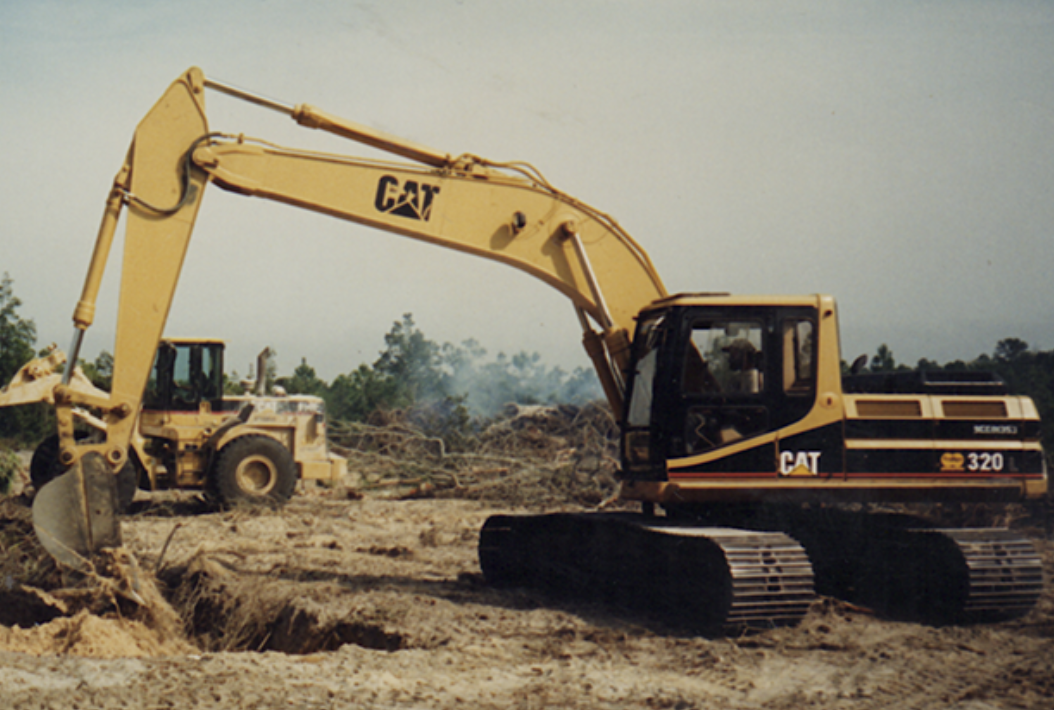 Construction site with a yellow Caterpillar excavator digging into the dirt, with another large machinery in the background.
