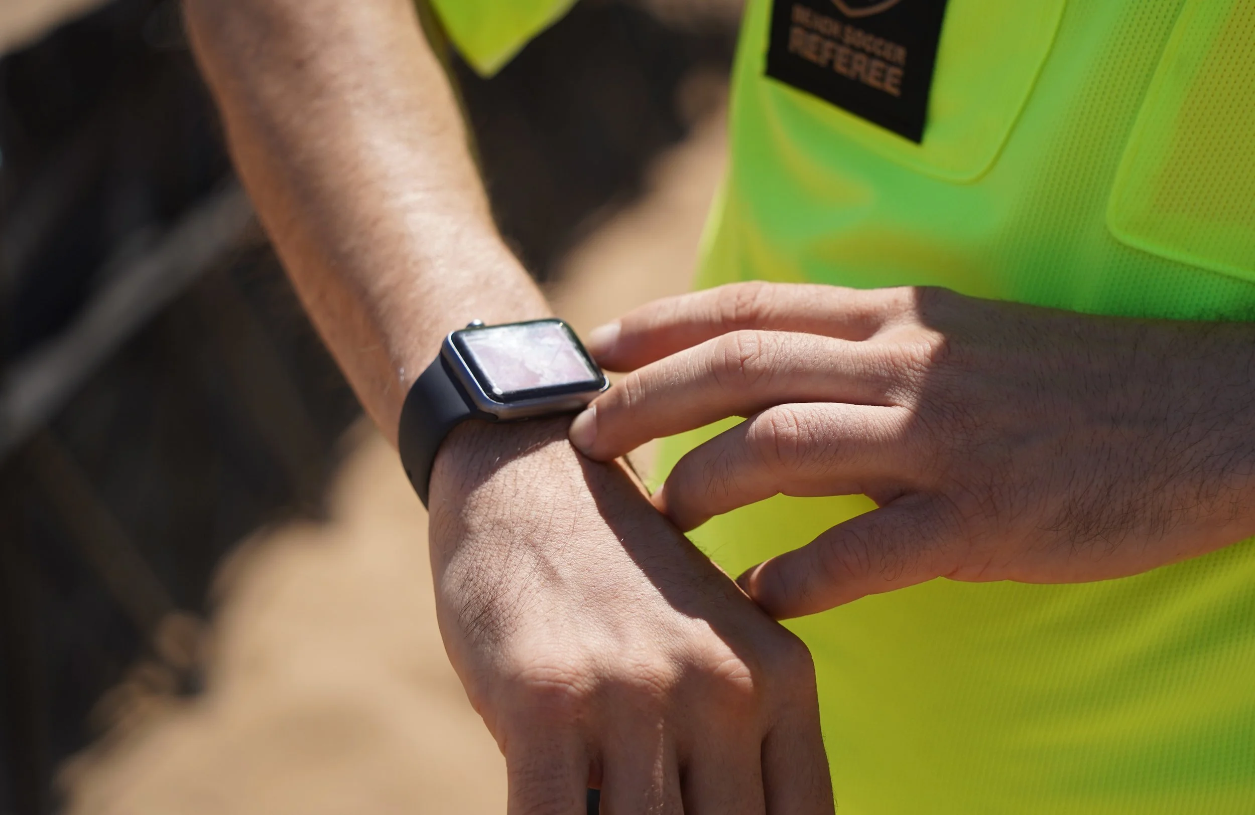 Close-up of a person in a neon yellow vest looking at a smartwatch on their wrist, outdoors on a sunny day.