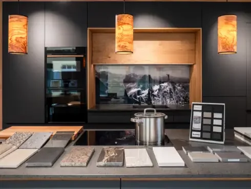 Moderne Küchenarbeitsplatte mit Mustern und Materialien, gedämpfter Wasserkocher, Musterbücher, schwarzer Wandanstrich und drei orange Lampen