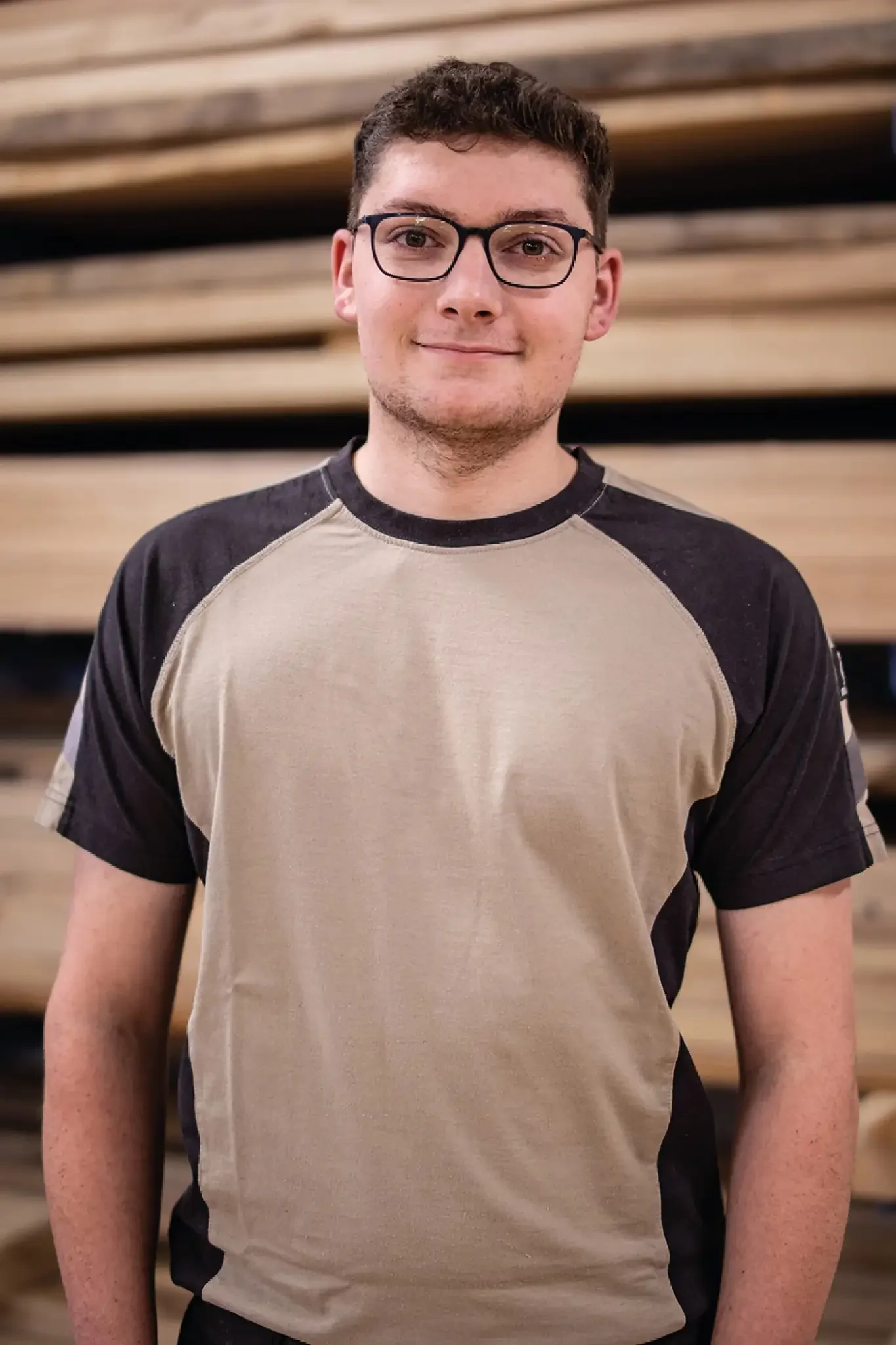 Halb-Körper-Portrait von Max im Holzquadrat T-Shirt vor aufeinander gestapelten Brettern