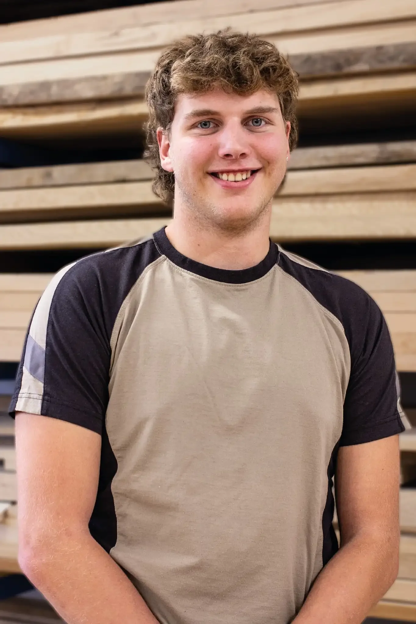 Halb-Körper-Portrait von Clemens im Holzquadrat T-Shirt vor aufeinander gestapelten Brettern