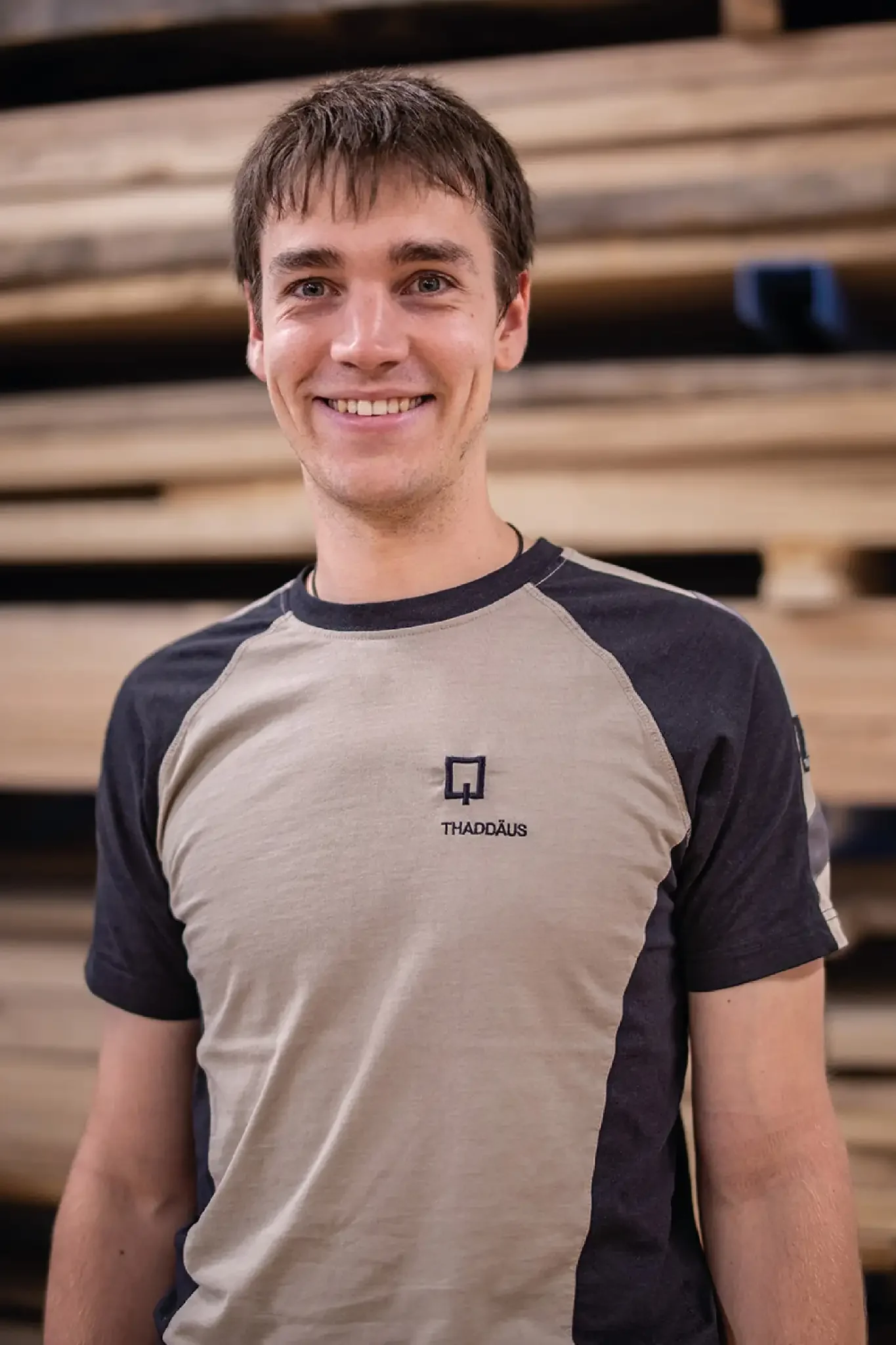 Halb-Körper-Portrait von Thaddäus im Holzquadrat T-Shirt vor aufeinander gestapelten Brettern