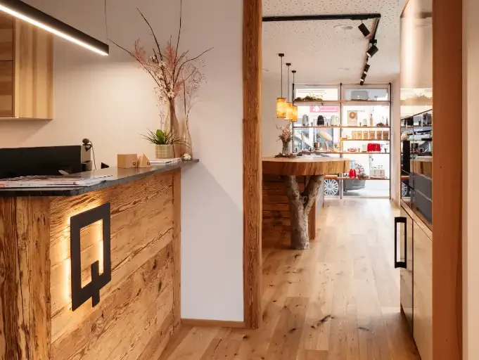 Innenraum des Holzquadrat Küchenateliers mit Holzregalen, einem Tresen aus Altholz und dekorativen Elementen wie Pflanzen und Lampen.