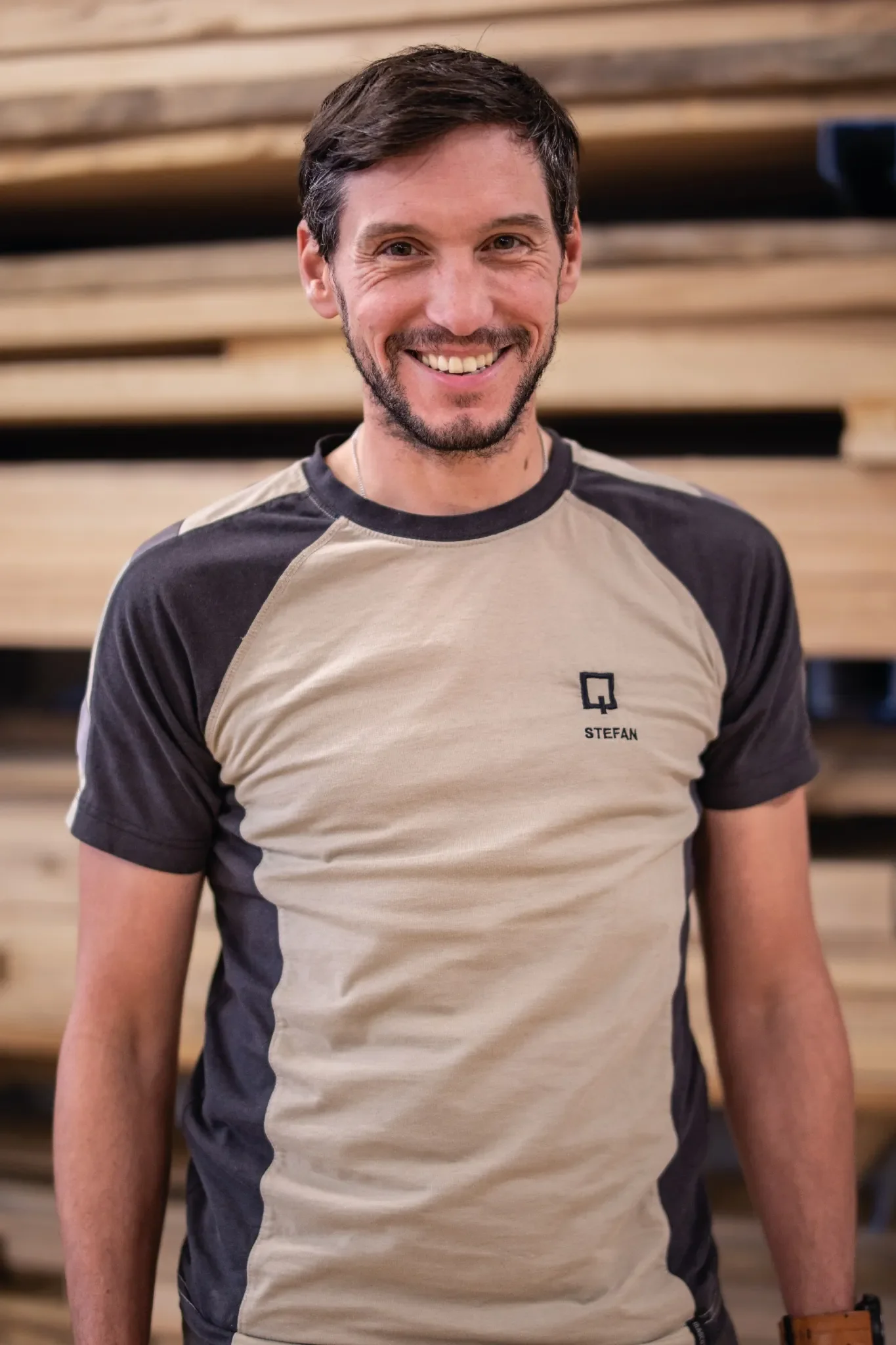 Halb-Körper-Portrait von Stefan im Holzquadrat T-Shirt vor aufeinander gestapelten Brettern