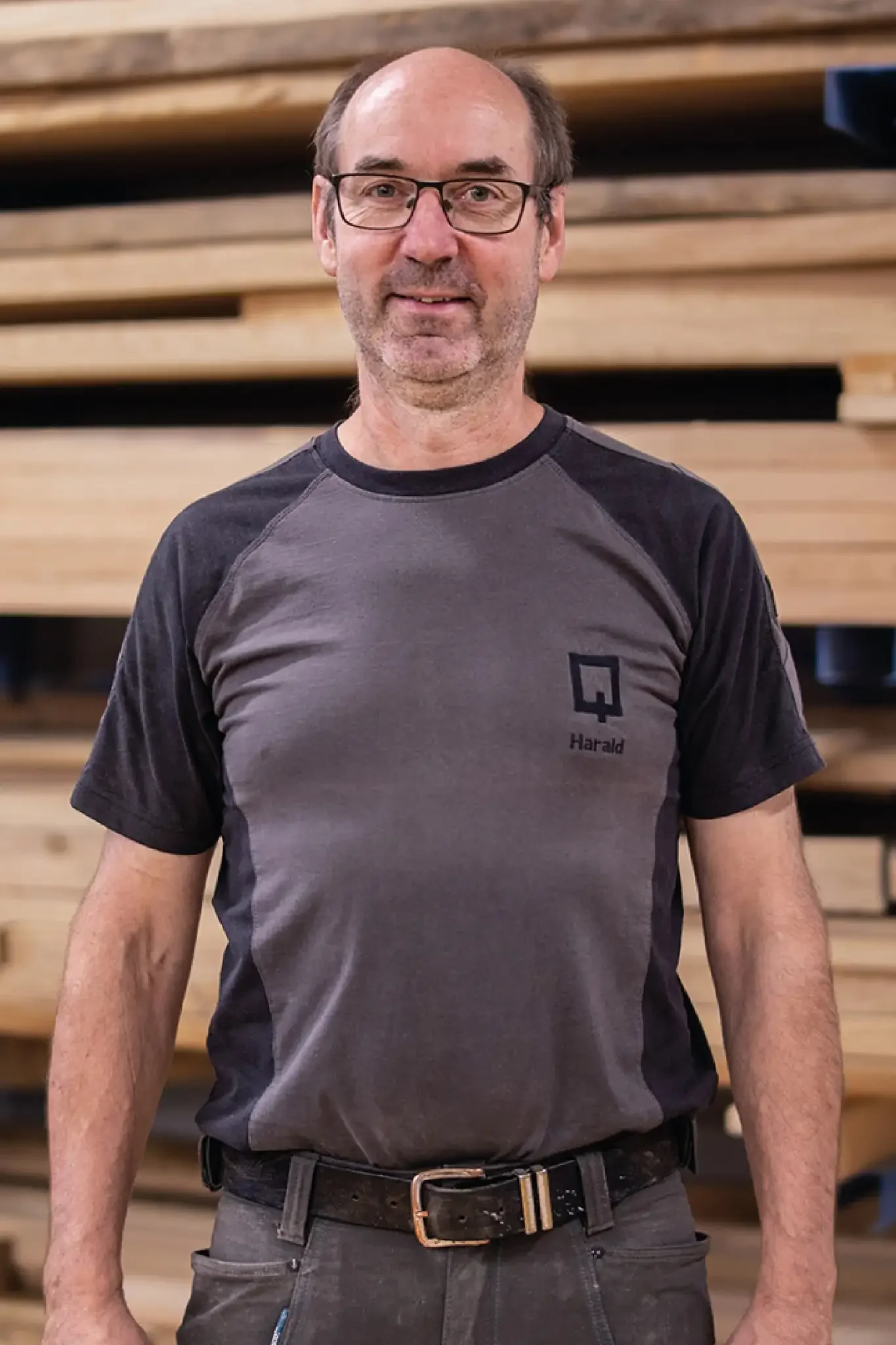 Halb-Körper-Portrait von Harald im Holzquadrat T-Shirt vor aufeinander gestapelten Brettern