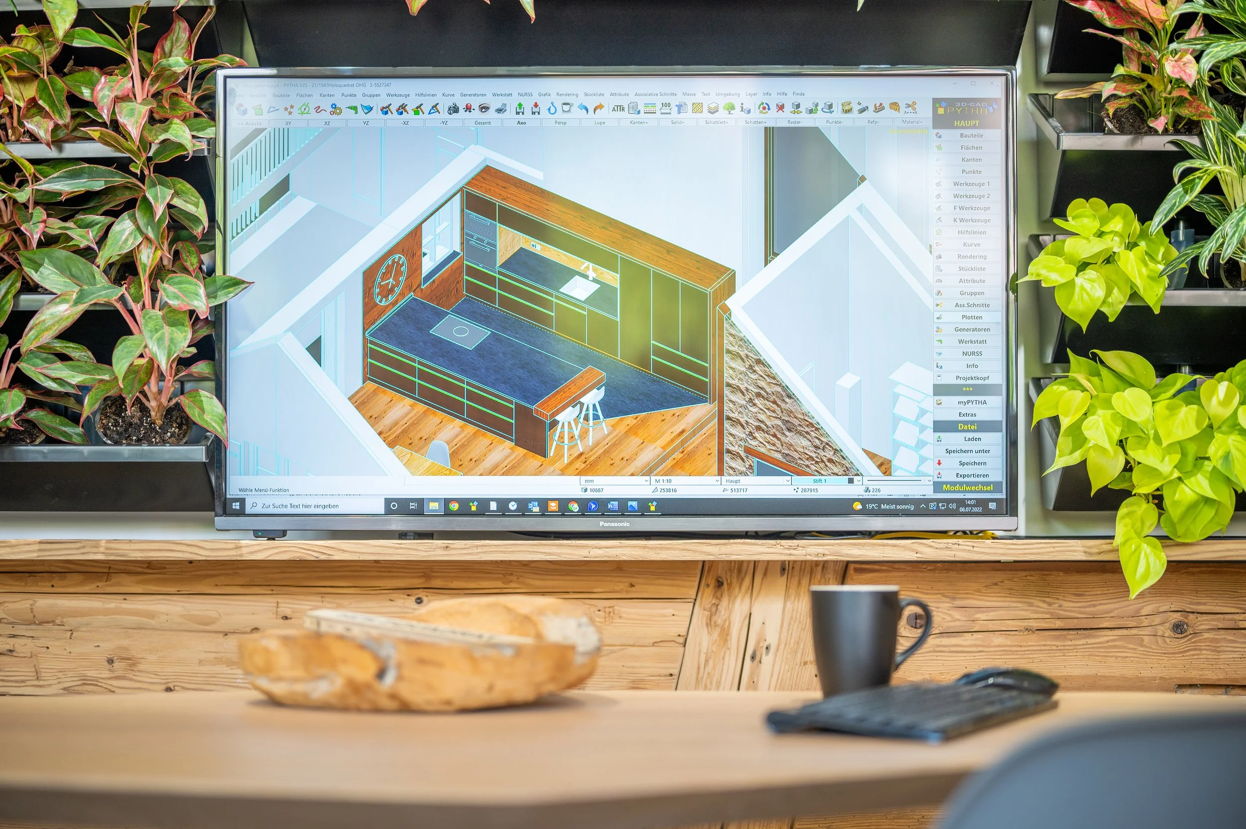 Computerbildschirm mit 3D-Design einer modernen Küche, umgeben von Pflanzen und einem Holztisch mit einer Schale, einer Tasse und einer Tastatur.