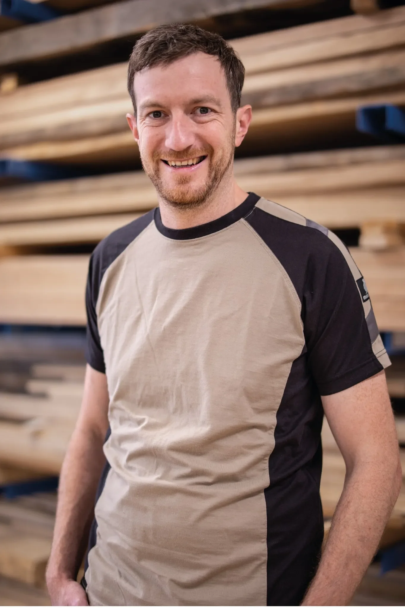 Halb-Körper-Portrait von Dominik im Holzquadrat T-Shirt vor aufeinander gestapelten Brettern