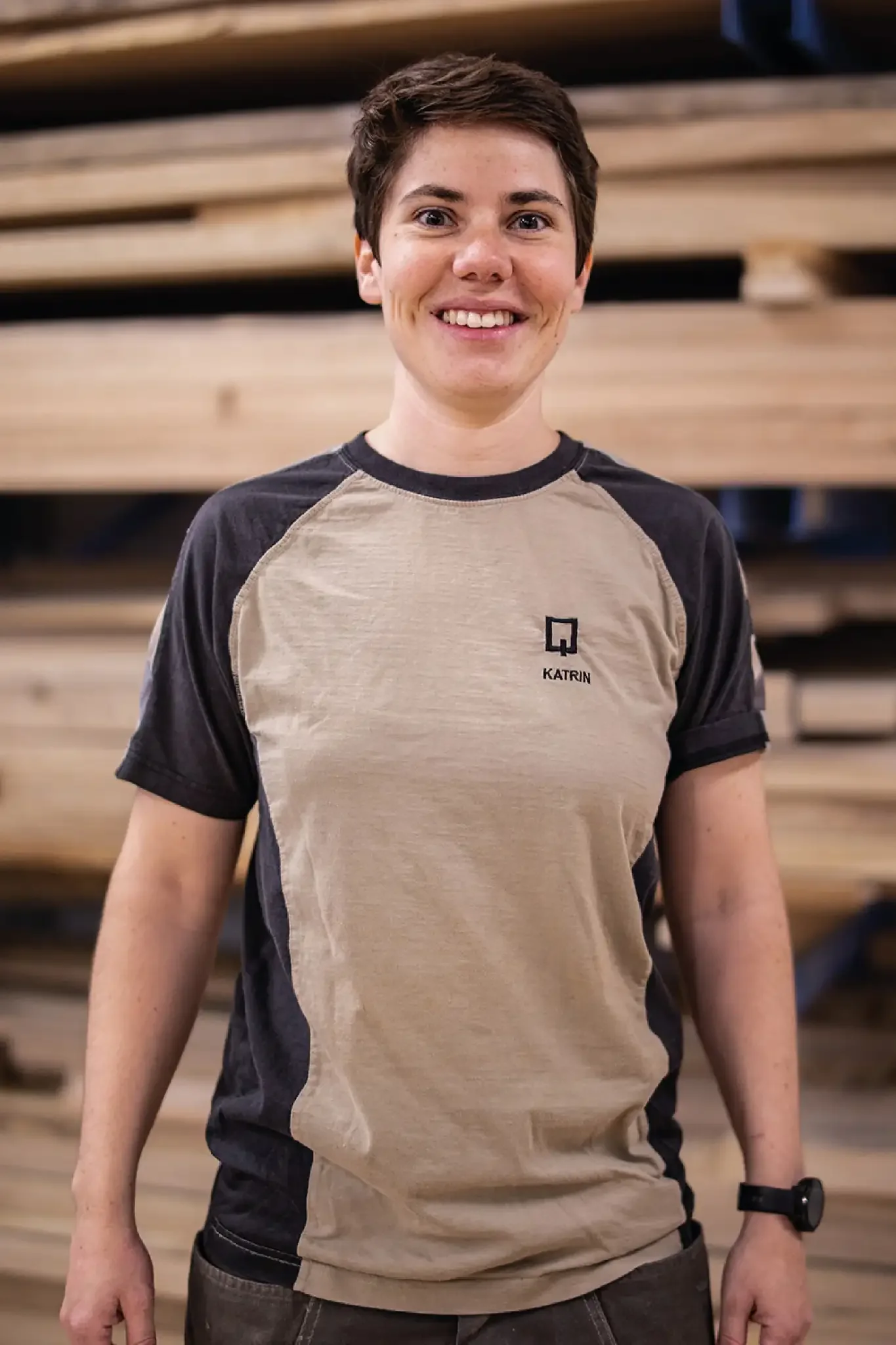 Halb-Körper-Portrait von Katrin im Holzquadrat T-Shirt vor aufeinander gestapelten Brettern