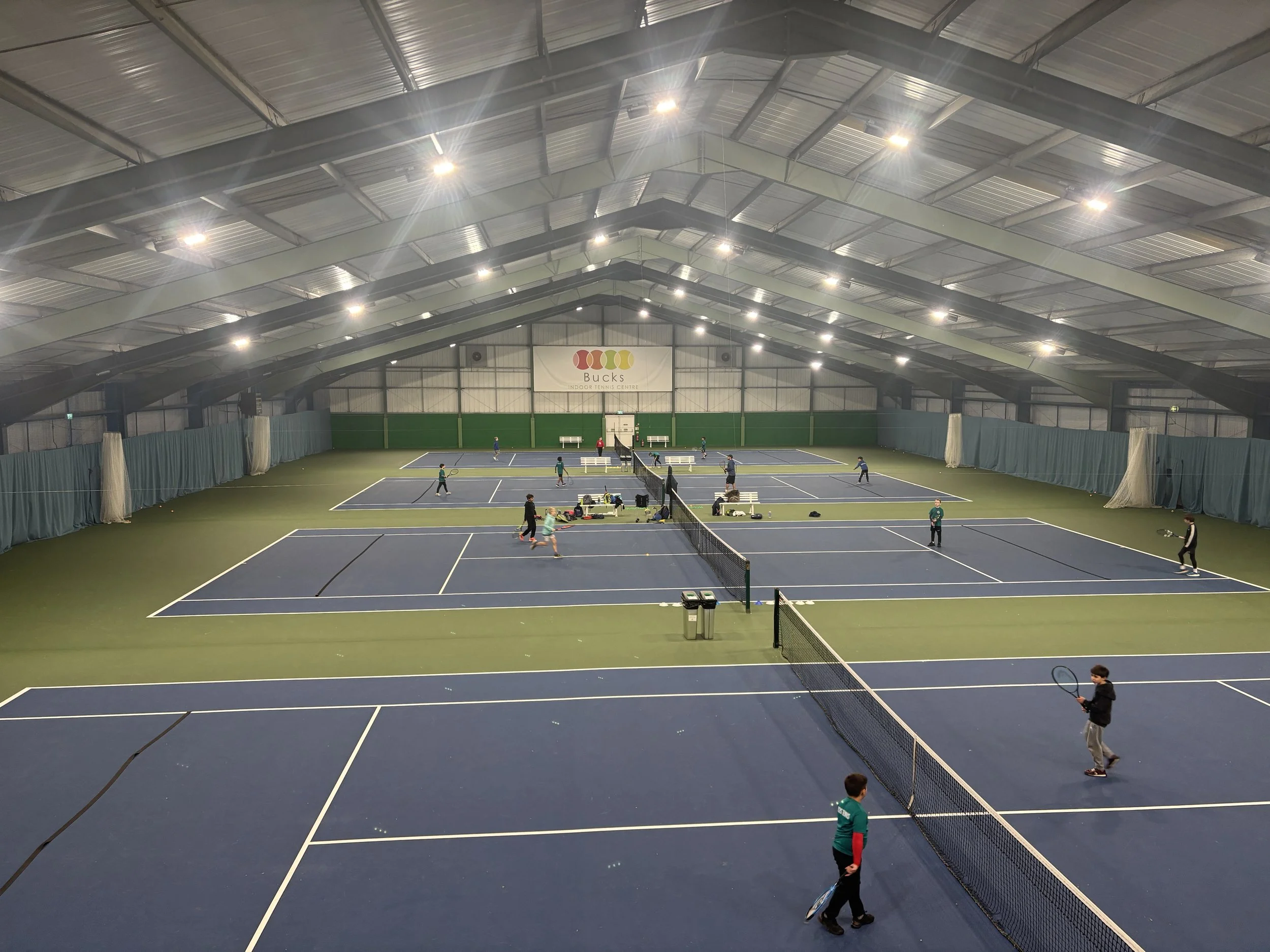 Bucks Indoor tennis court with multiple game areas, players practicing, and a Bucks sign on the background.