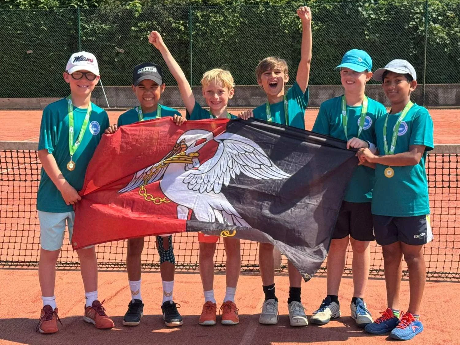 Bucks Indoor County Tennis players on a tennis court holding a flag of Poland, celebrating with medals around their necks.