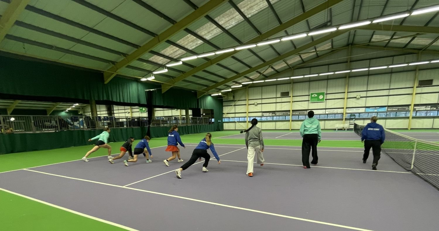 Under 18 Bucks County Girls people playing tennis indoors, warming up near the net.