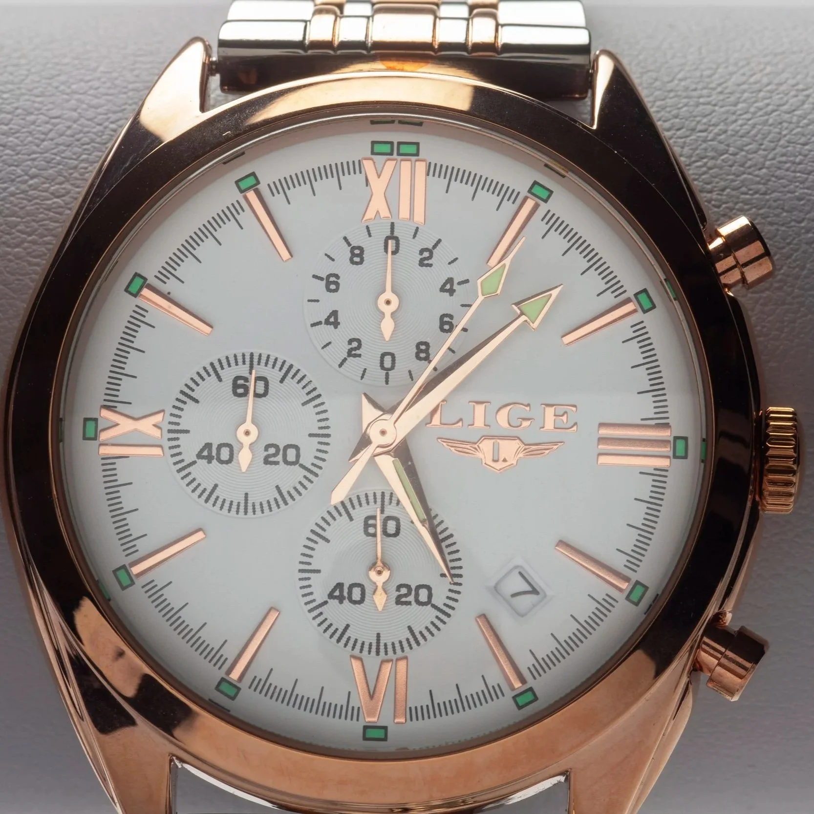 Close-up of a LIGE men's wristwatch with a white face, rose gold case, and a chronograph dial showing time, seconds, and minutes, with a date window at 4 o'clock.