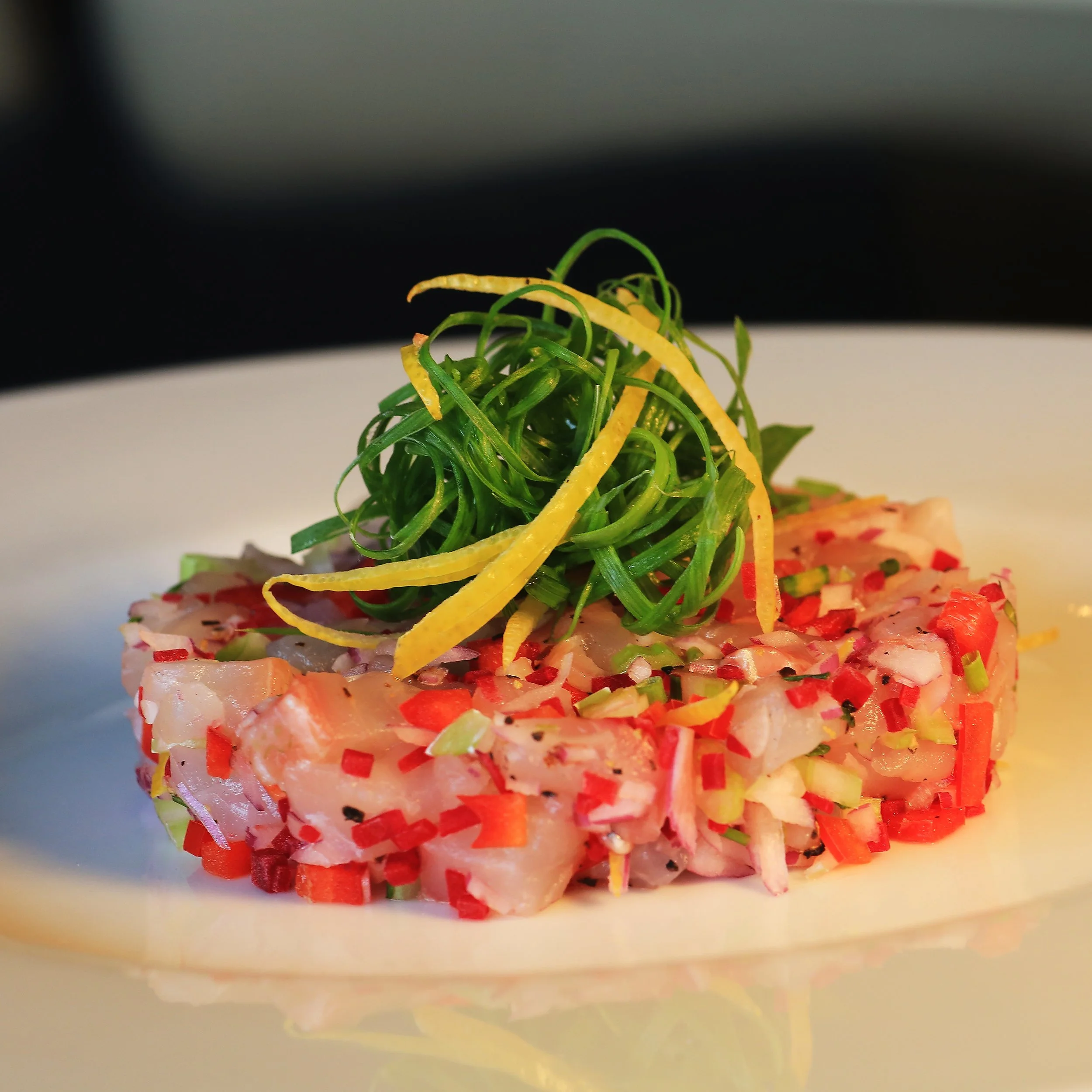 Beautifully plated fish tartare made with tender diced white fish, crisp red peppers, red onion, and green onion, finished with a vibrant garnish of curly green onion and thin strips of lemon zest. A fresh, light, and colorful appetizer perfect for f