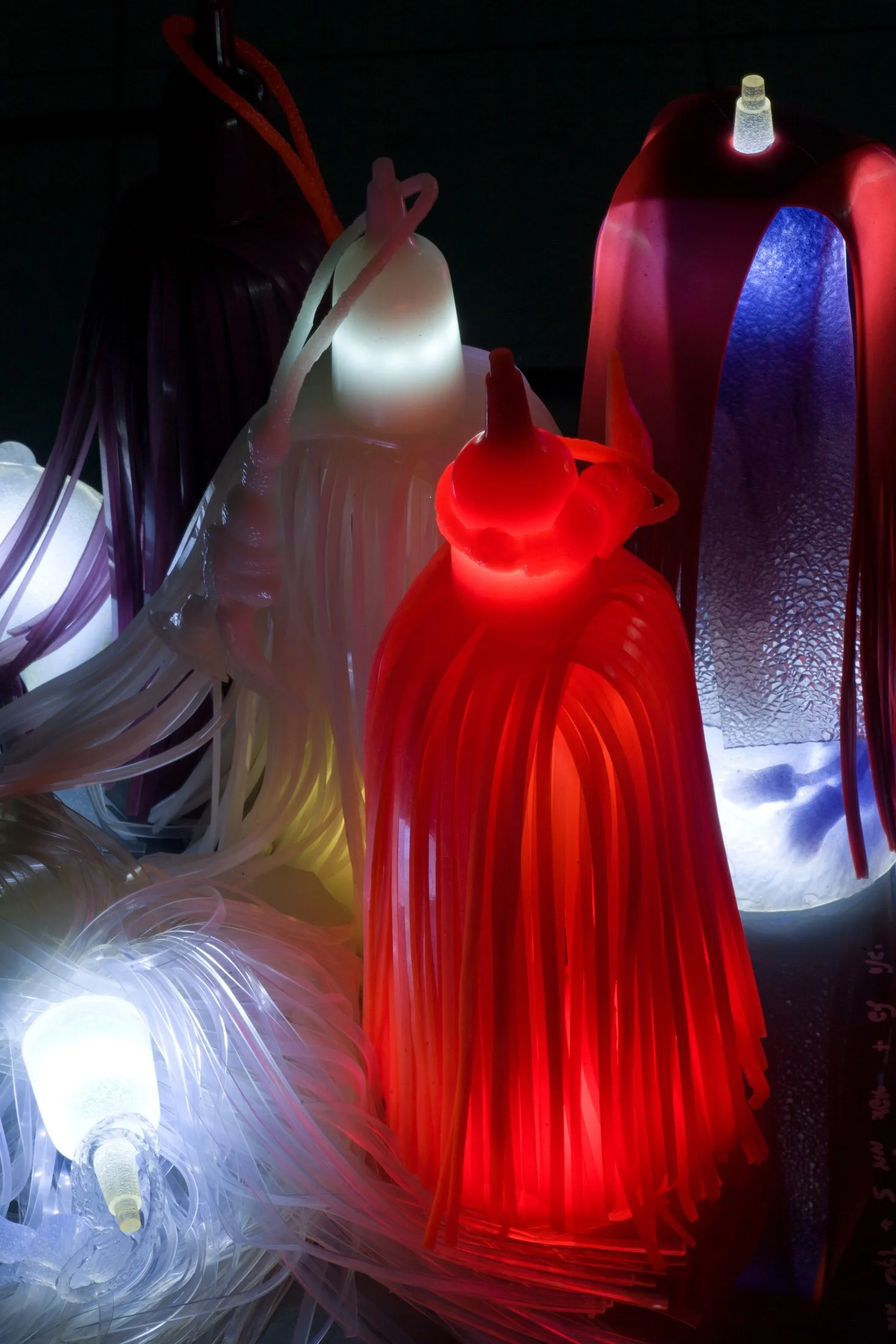 Colorful luminous art sculptures made of plastic, illuminated in red, white, purple, and blue, resembling abstract figures or objects.