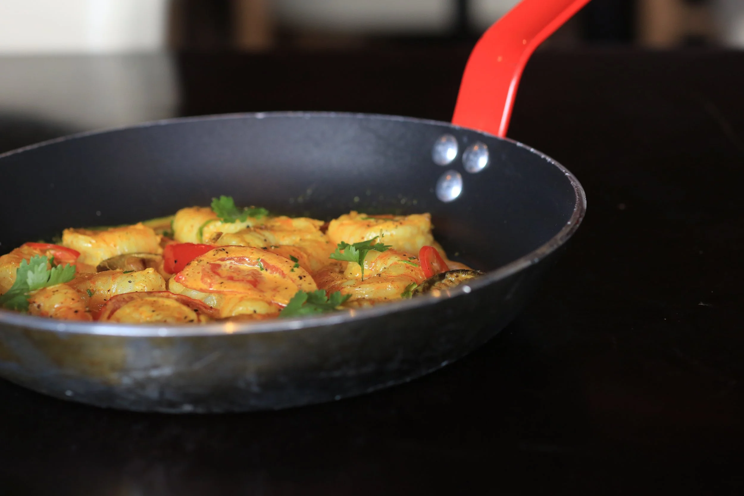 Sizzling creamy shrimp cooked in a black skillet with red chili slices and fresh cilantro garnish.