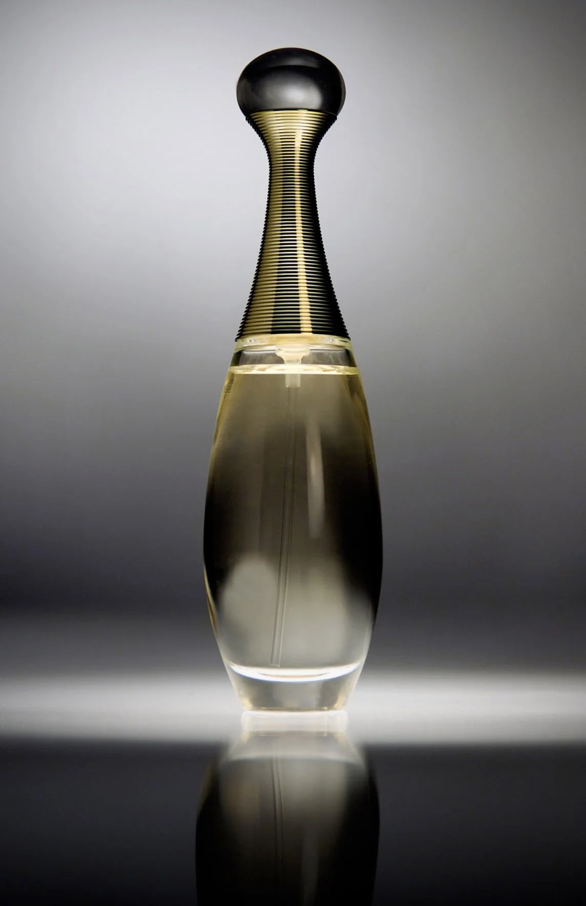 A modern, sleek glass perfume bottle with a black spherical cap, sitting on a reflective surface, against a neutral background.