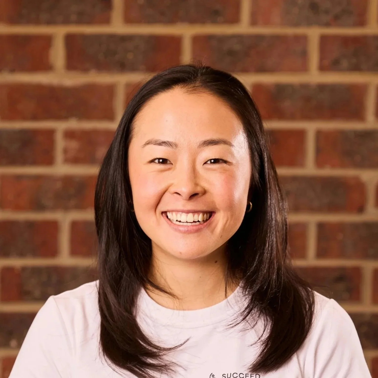 Smiling Asian woman with shoulder-length dark hair in front of a brick wall.
