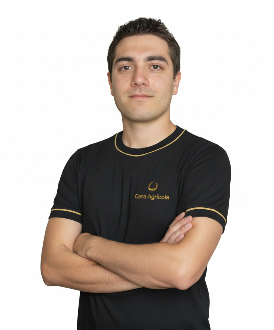 Jovem homem com cabelo castanho claro, pele clara, usando uma camiseta preta com detalhes dourados, com o logo da Cana Agrícola. Ele está com os braços cruzados e expressão confiante, branco de fundo.