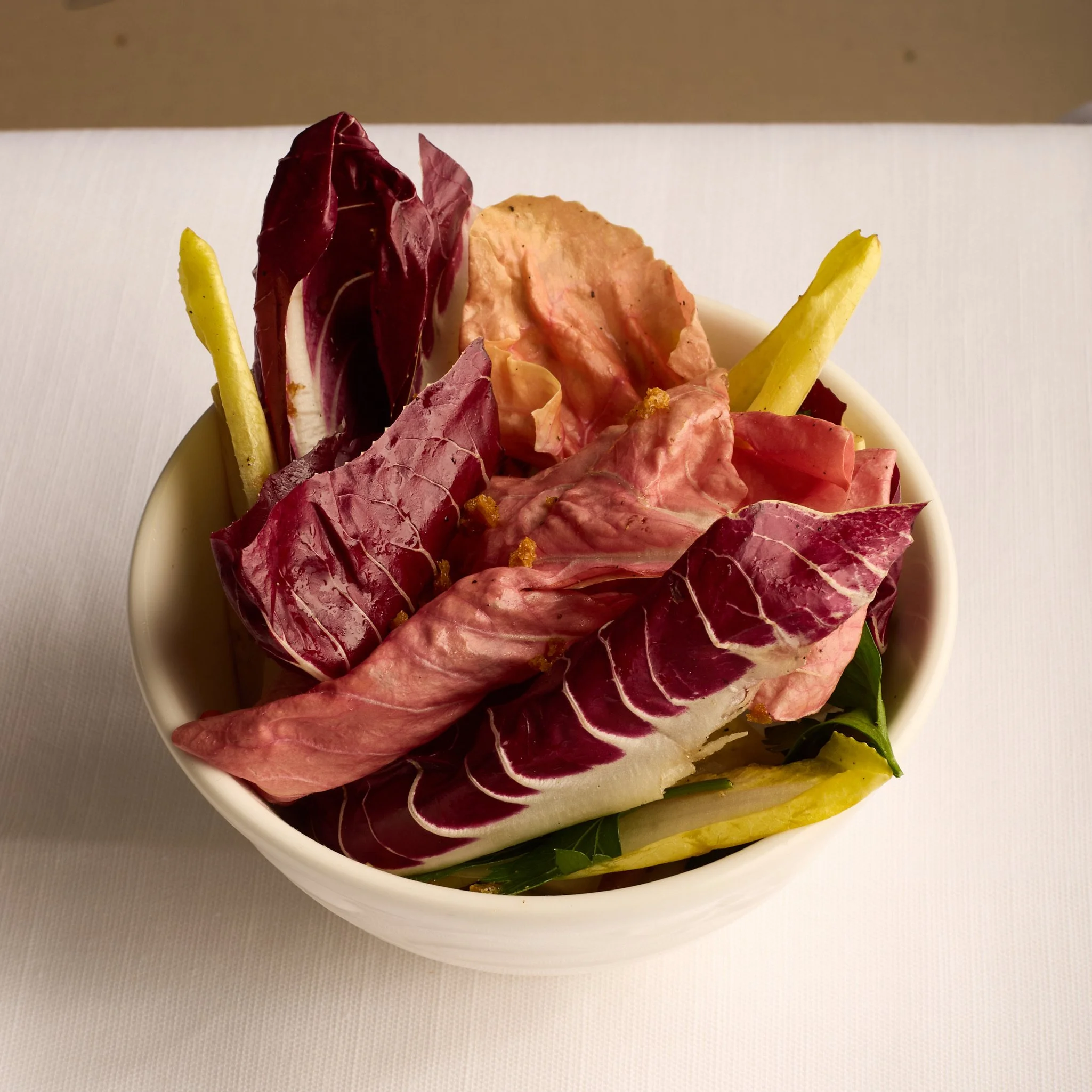 Assorted colorful radicchio salad in a white bowl on a white surface.
