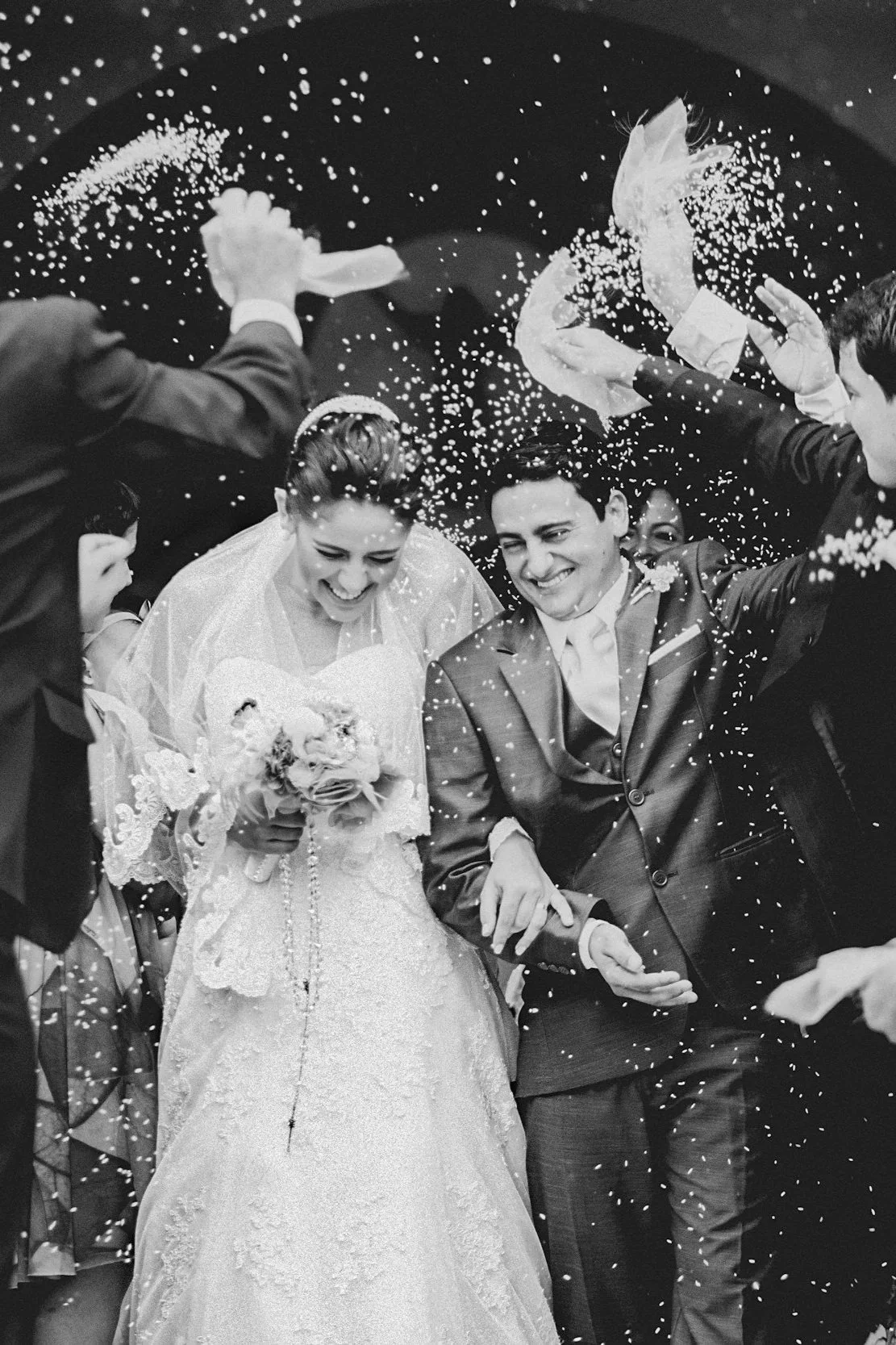 A wedding celebration with a bride and groom smiling and walking through showering confetti with joyful friends.