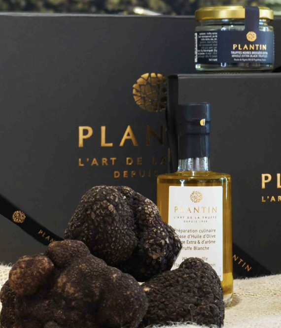 Autographed black box with gold lettering labeled 'PLANTIN' surrounded by black truffles, a bottle of black truffle oil, and a jar of black truffle spread.