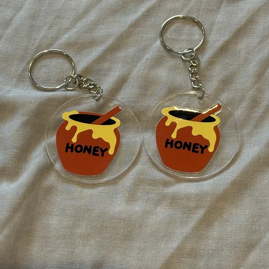 How cute are our new keyrings. 

Add a splash of whimsy to your everyday essentials with this quirky acrylic round keyring featuring a charming honeypot design. Perfectly petite and delightfully detailed, the glossy finish catches the light just righ