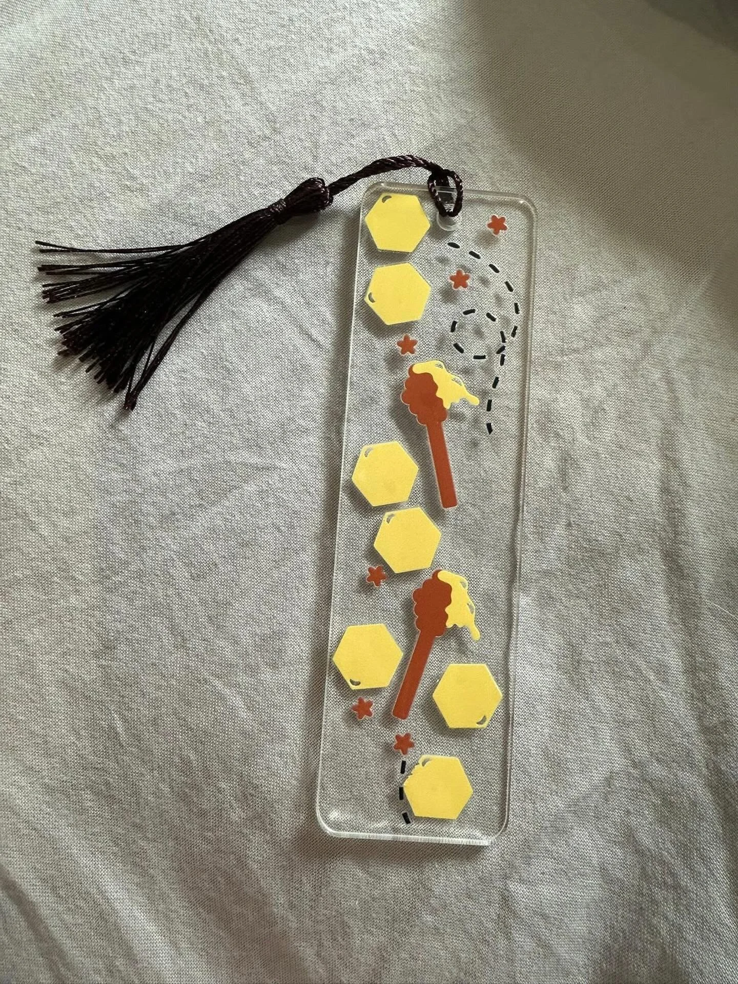 Buzzing into your reading life! 🐝
Introducing our adorable Honeycomb Delight Acrylic Bookmark&mdash;the perfect way to save your spot.
Made from durable, clear acrylic and featuring cute honey dippers and a luxe dark tassel. It&rsquo;s thin enough t