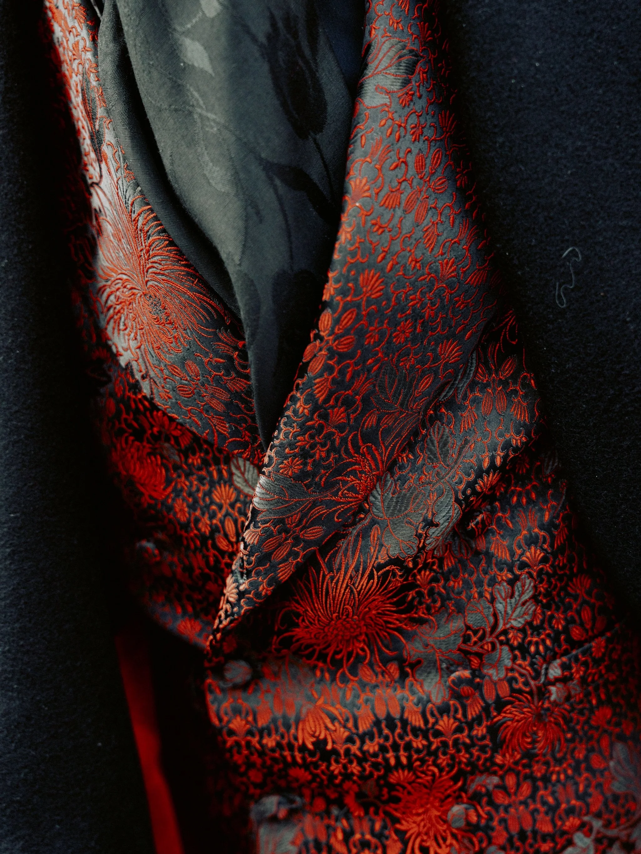 Close-up of a black floral-patterned scarf with red and orange floral designs, draped over a black coat.